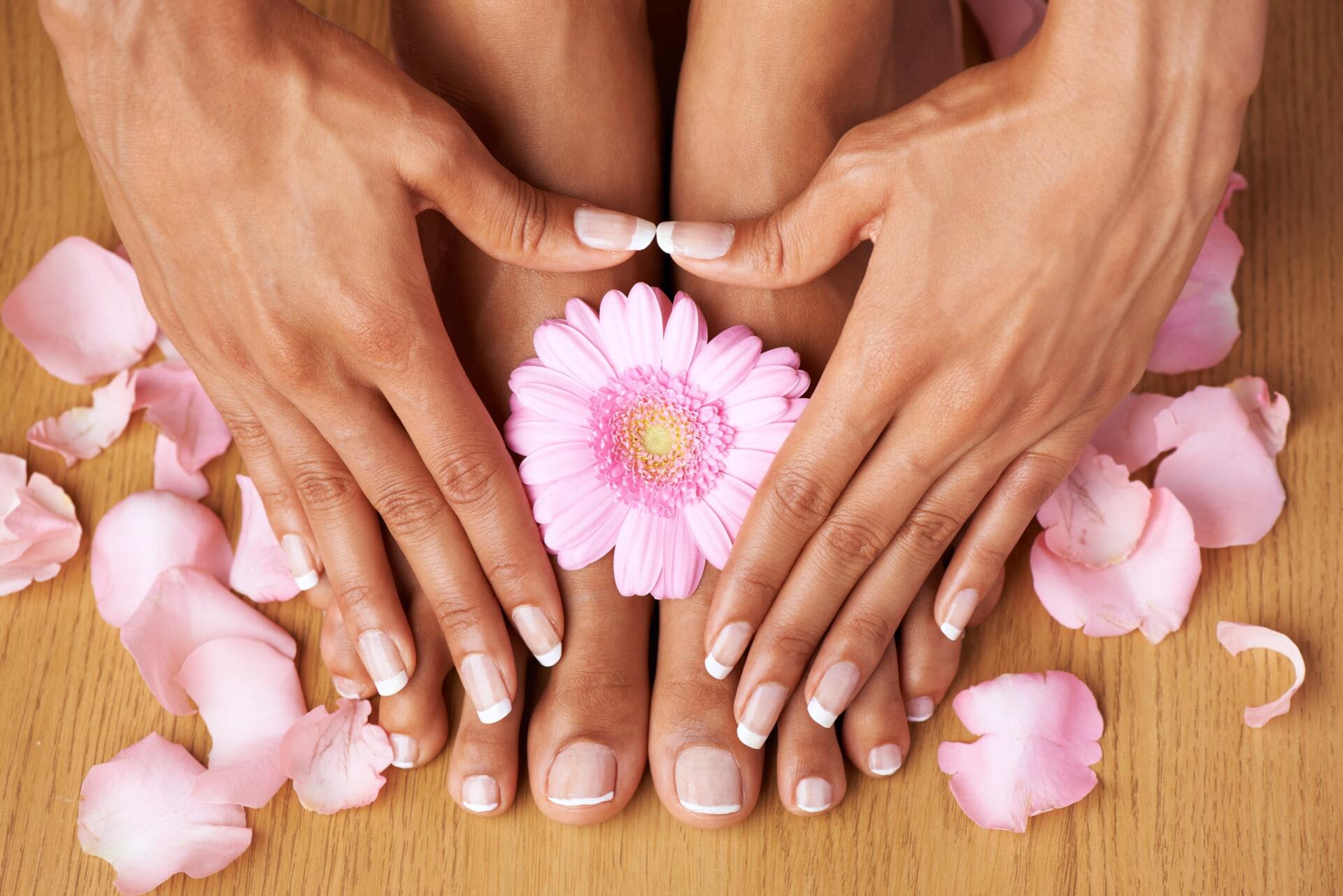 Mani e piedi con petali rosa e un fiore su una superficie di legno.