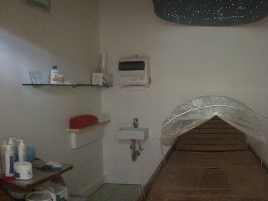 Sala trattamenti in salone con lettino da massaggio e scaffali per le attrezzature, coperta da una tettoia in plastica traslucida.