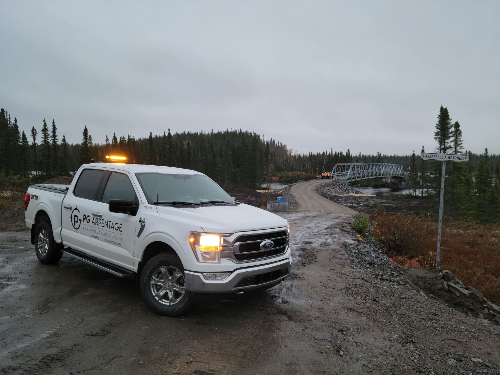 Camionnette blanche avec gyrophare orange sur une route boueuse dans une zone rurale nuageuse