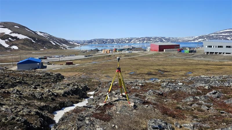 Trépied de levé dans un paysage arctique enneigé avec des bâtiments et des montagnes à l'horizon