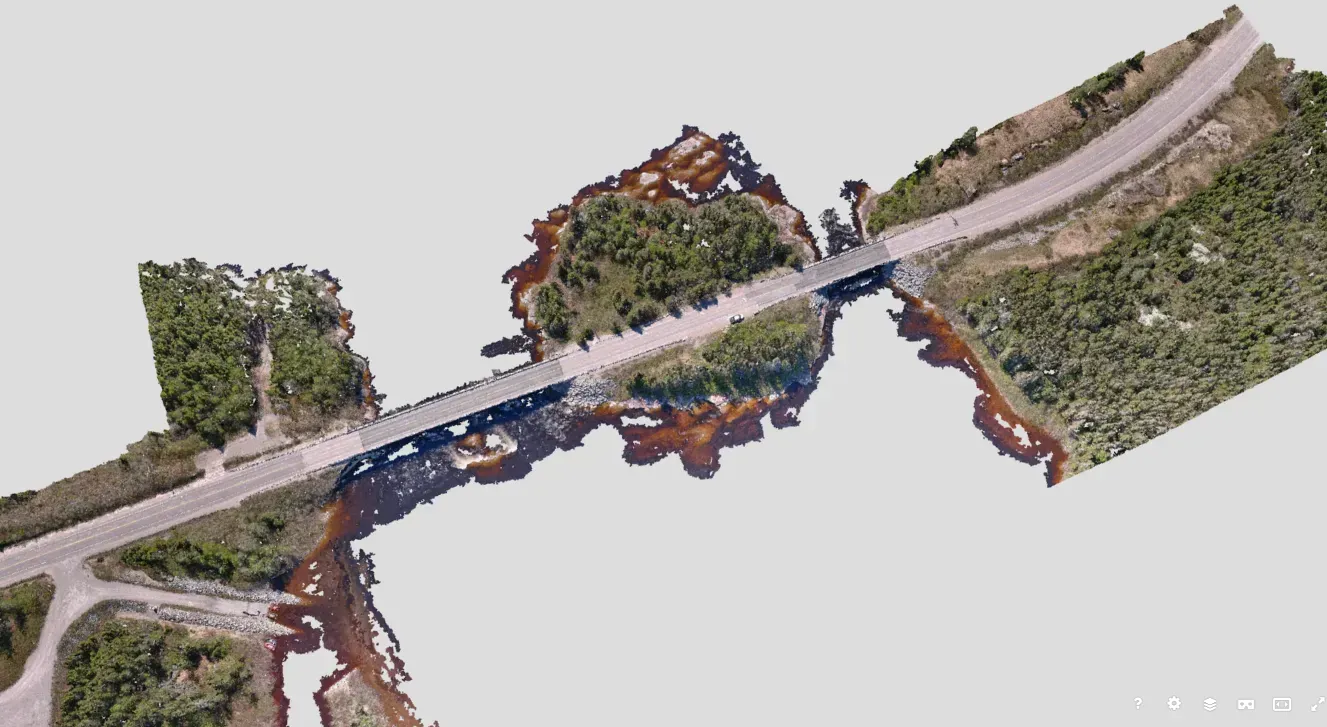 Une image aérienne 3D en plongée montre un pont enjambant un cours d'eau étroit et sombre, entouré d'une végétation luxuriante.