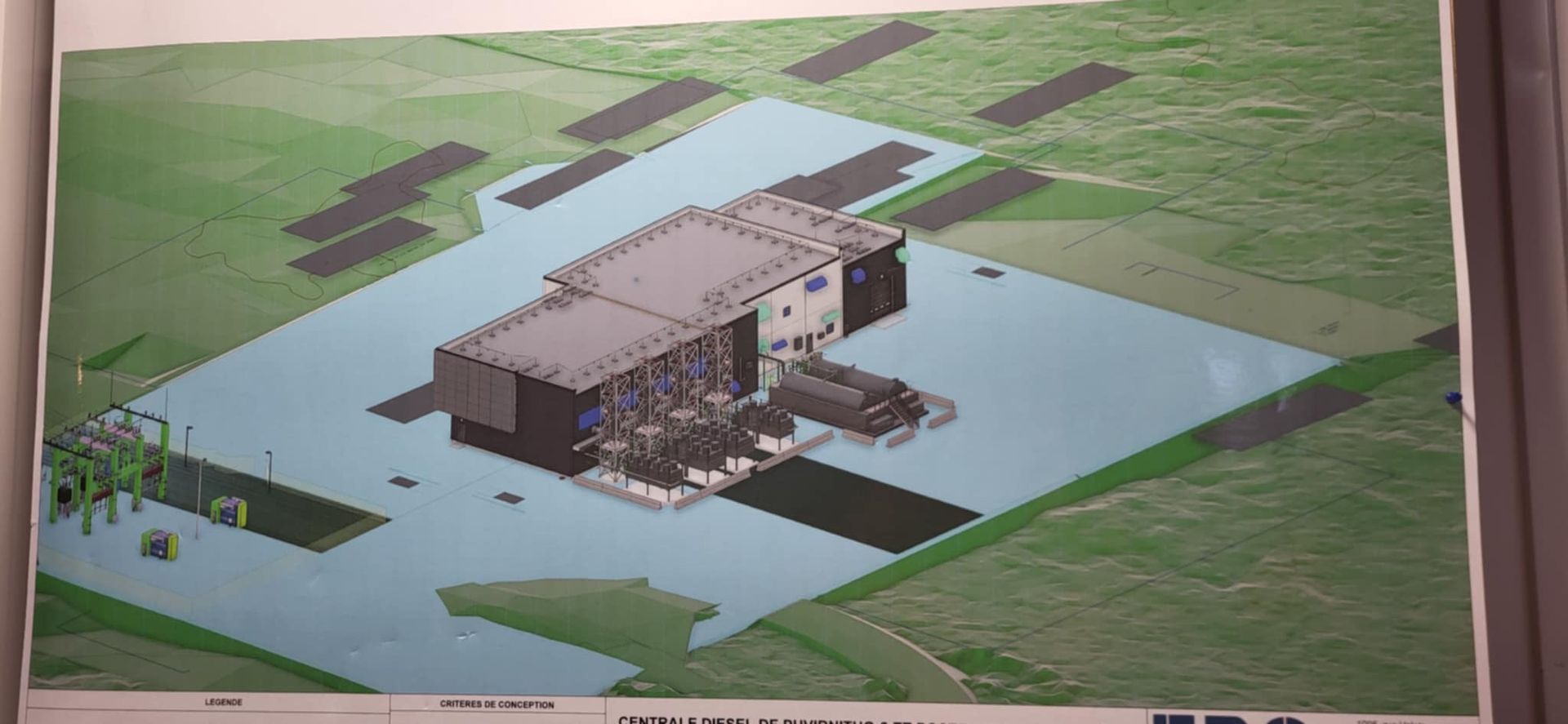 Une représentation isométrique montre un entrepôt industriel entouré d'une surface bleu clair, se détachant sur un champ vert.