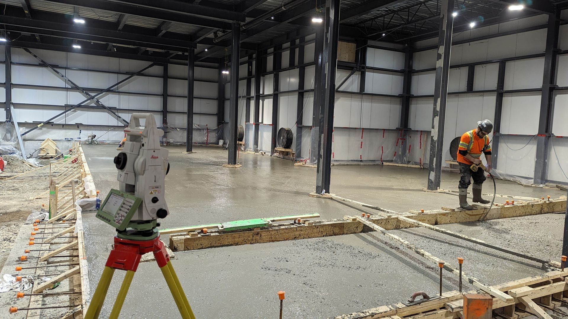 Théodolite laser sur trépied et ouvrier avec équipement de nivellement sur chantier intérieur.