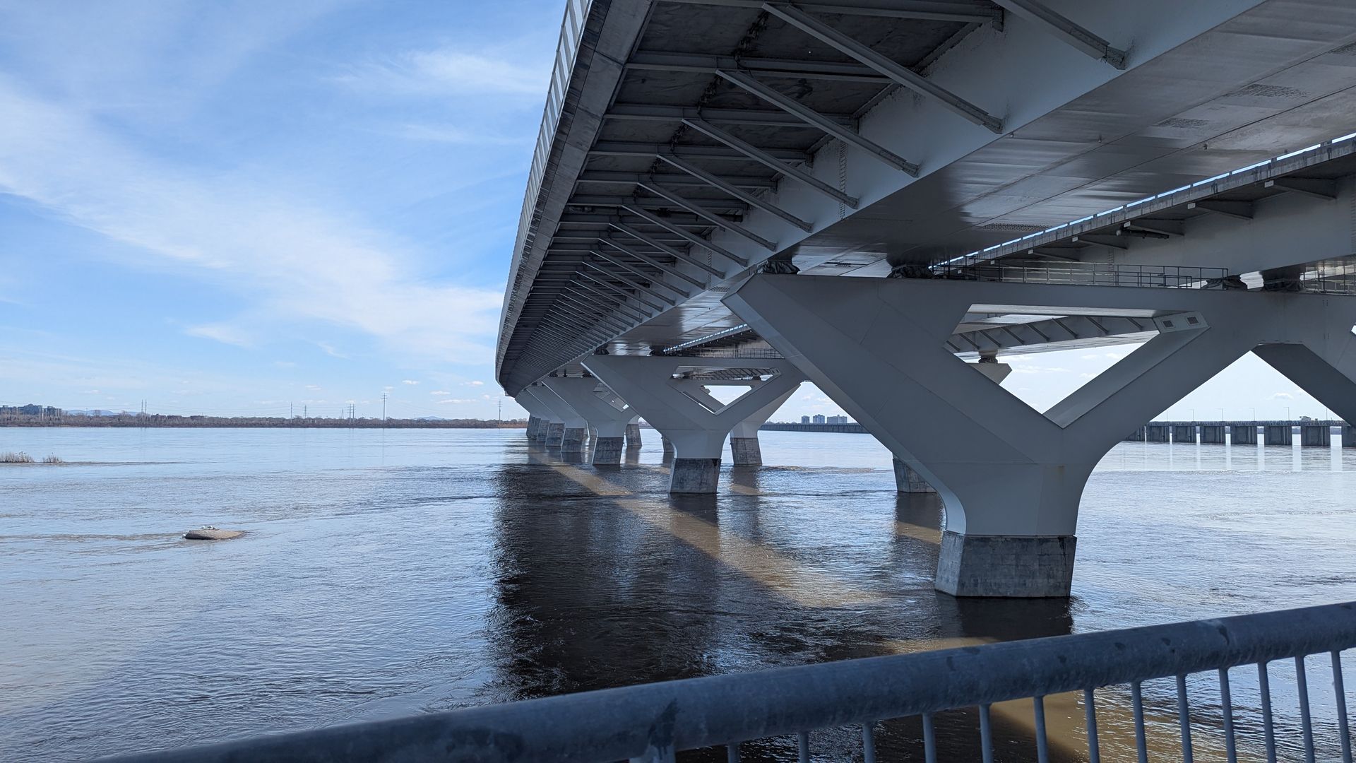 Rive enneigée sous un grand pont aux supports en béton et à la rambarde métallique au premier plan