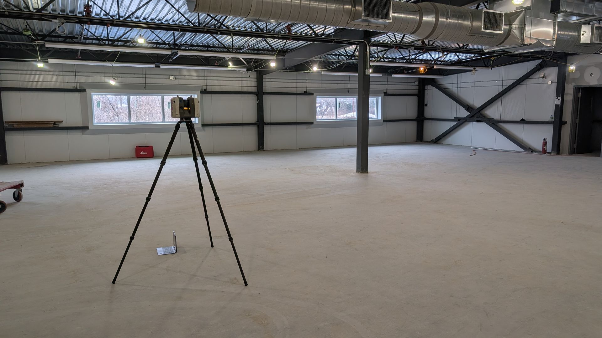 Entrepôt industriel vide avec une caméra sur trépied au premier plan et des poutres apparentes au plafond
