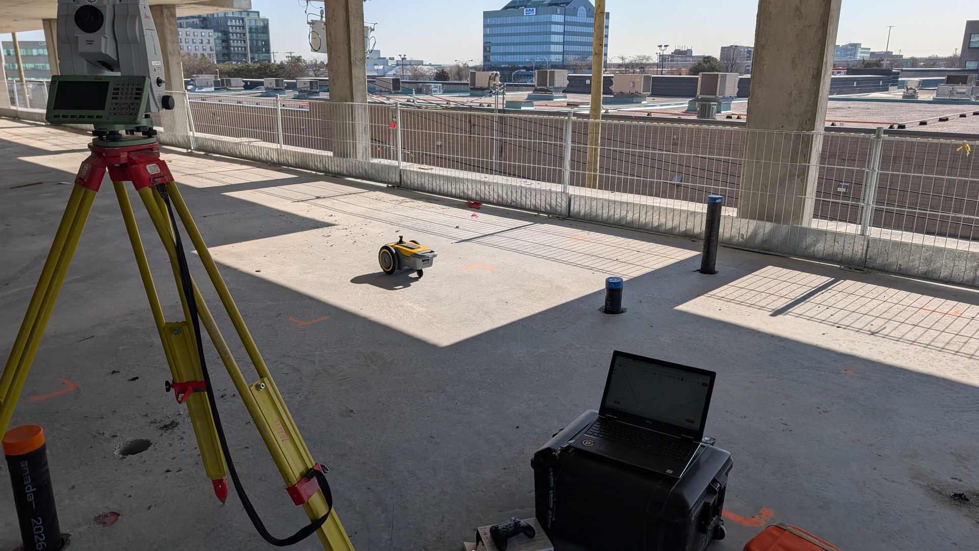 Une station totale sur trépied et un ordinateur portable dans une sacoche, installés pour effectuer des relevés topographiques sur un sol en béton.