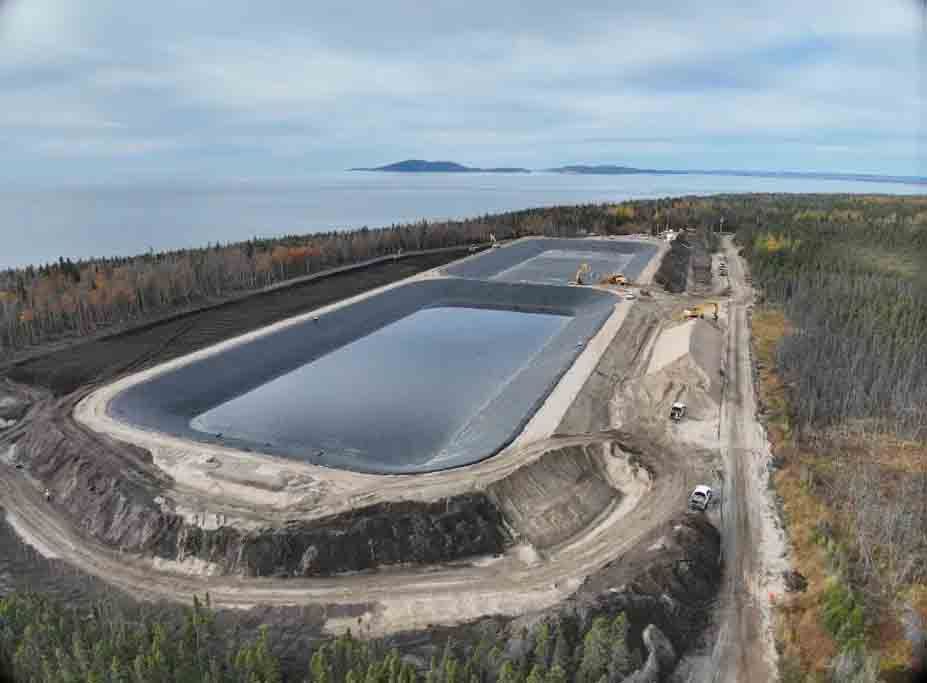 Vue aérienne de deux grands bassins de stockage d'eau revêtus, situés sur une côte boisée à proximité d'un plan d'eau.