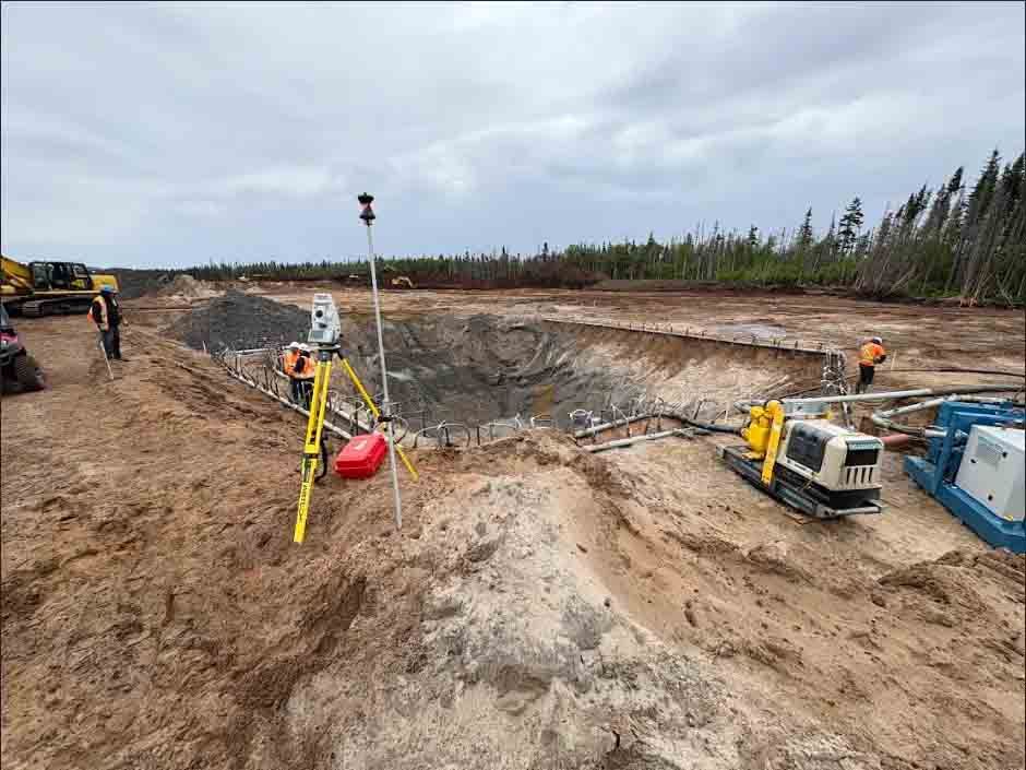 Ouvriers et matériel topographique sur un chantier de construction en extérieur comportant une grande fosse excavée et des engins lourds.