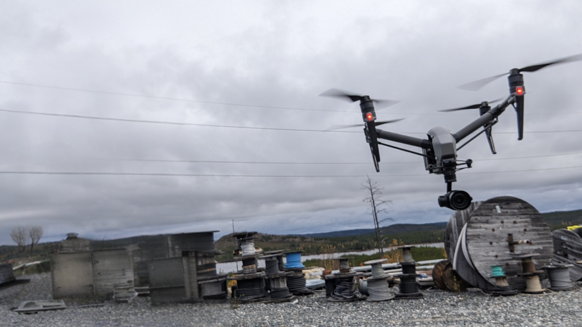 Un gros drone survole un toit avec des équipements métalliques et un ciel nuageux en arrière-plan.