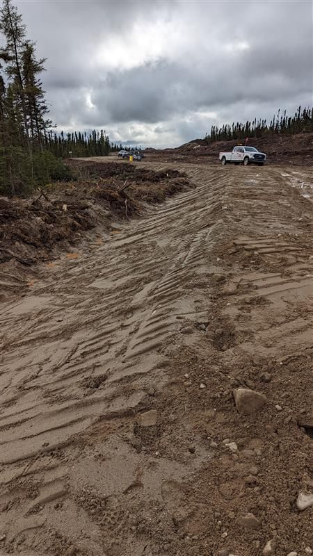 Chemin de terre sous un ciel nuageux, avec une camionnette blanche sur le côté droit d'un paysage rocailleux dégagé.