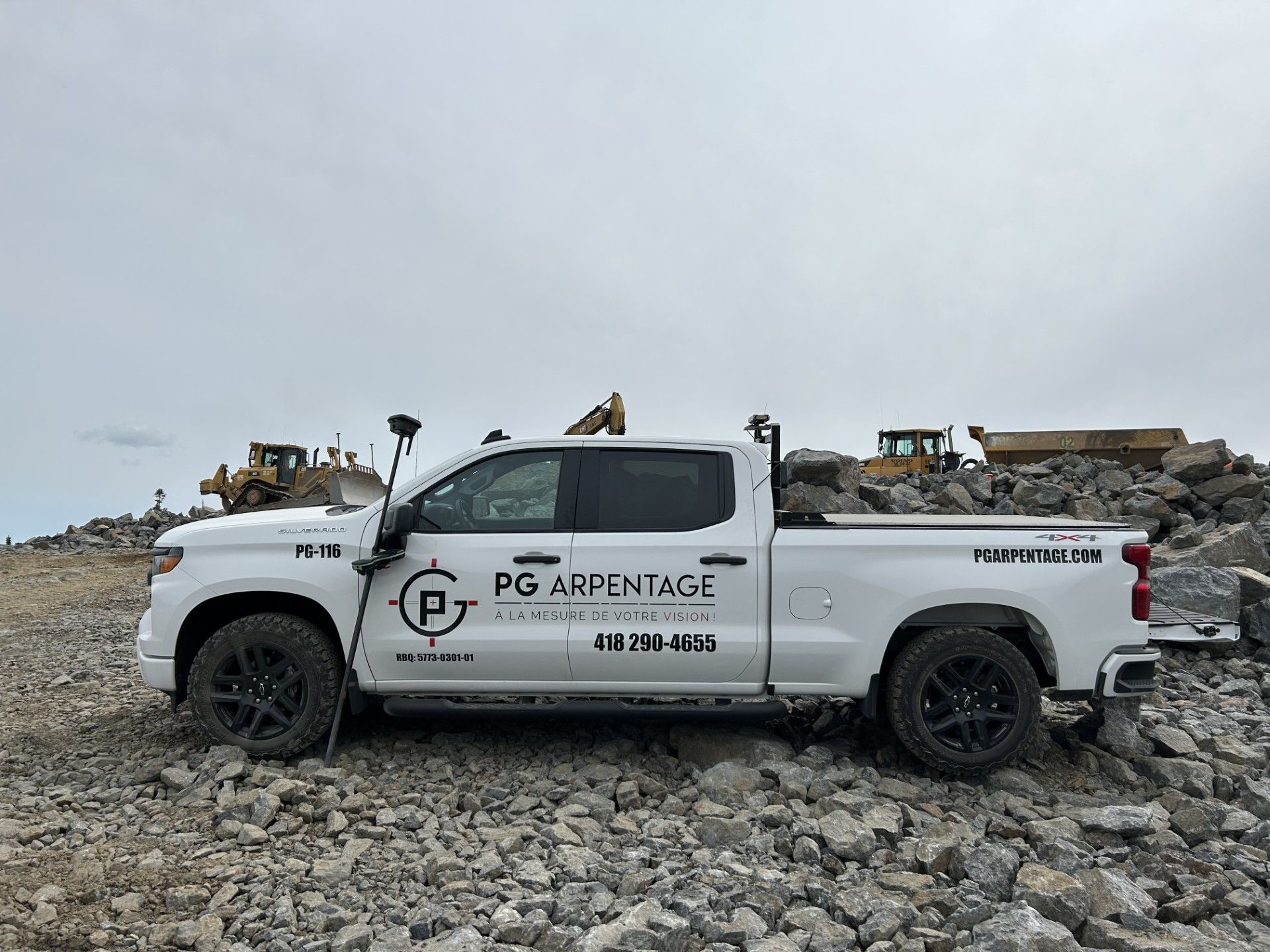 Une camionnette blanche portant le logo « PG AIR IMAGE » est garée sur un terrain rocailleux sous un ciel nuageux.