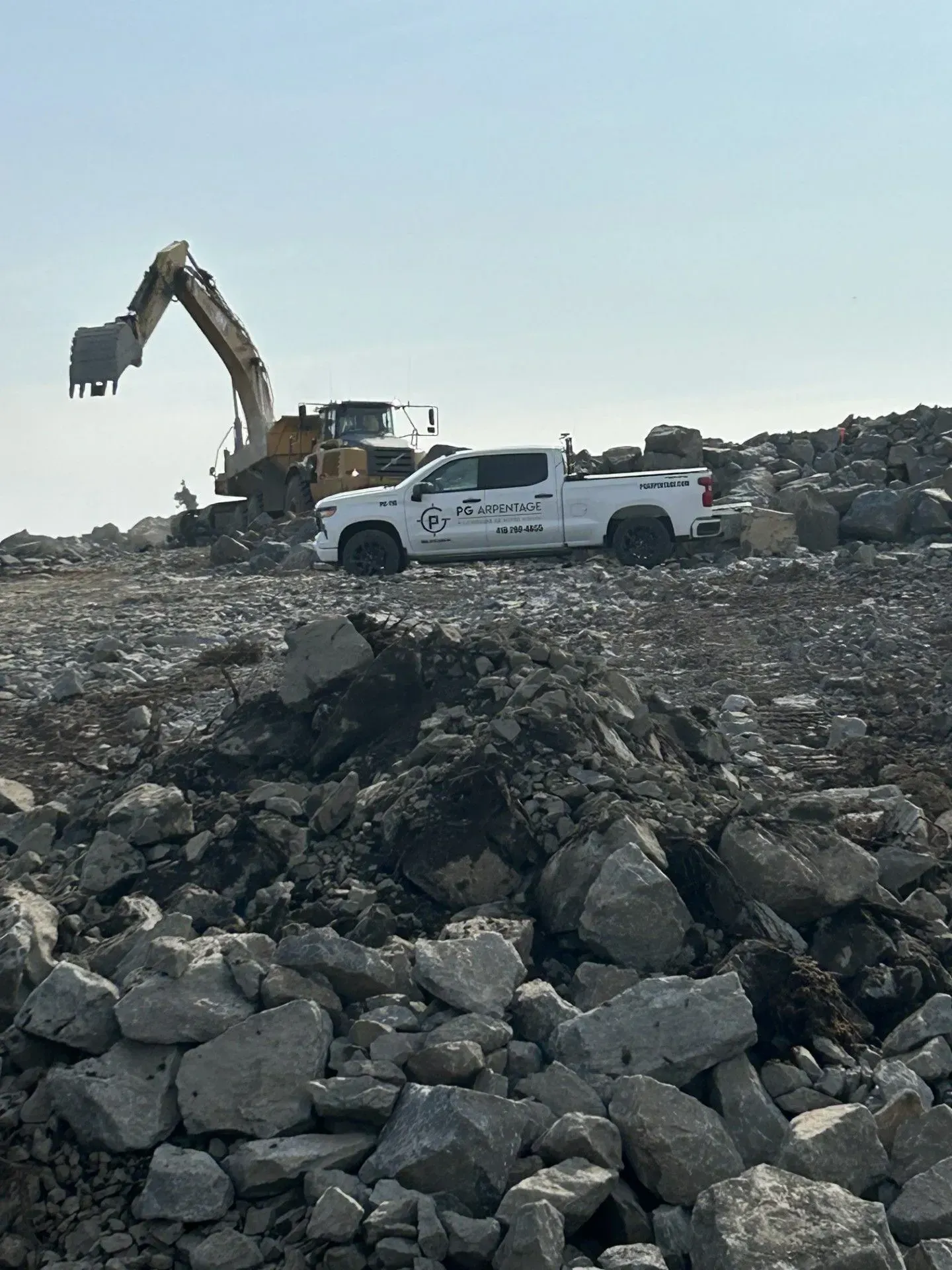 Une excavatrice et une camionnette blanche sur un chantier rocailleux sous un ciel dégagé