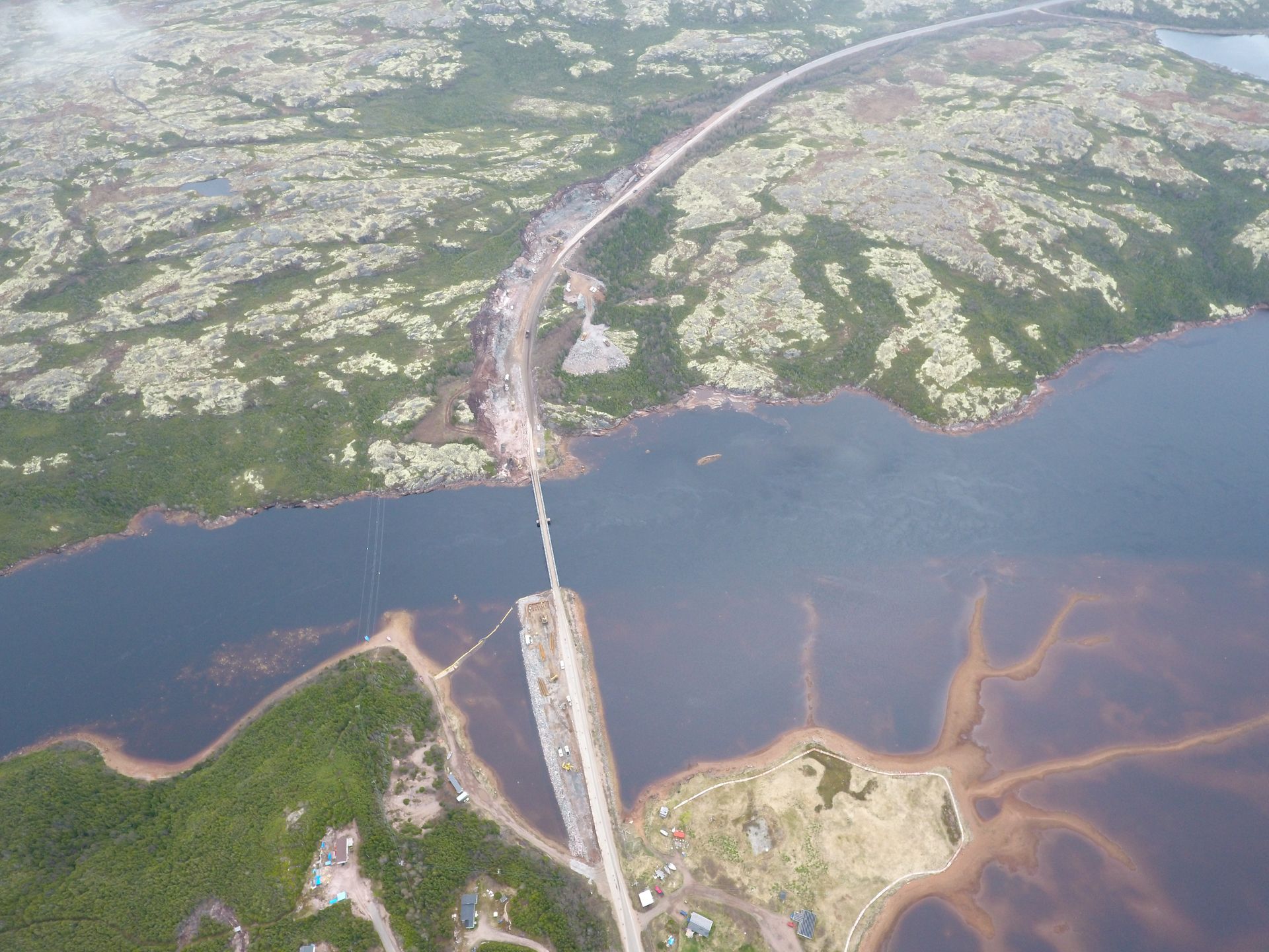 Vue aérienne d'un pont enjambant une large rivière, avec des terres verdoyantes et une rive boueuse en contrebas.