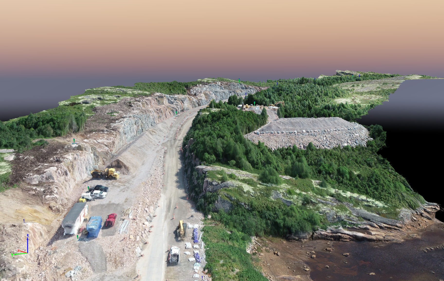 Vue aérienne d'une route de carrière rocheuse avec des engins de chantier et de la végétation verte le long du rivage.