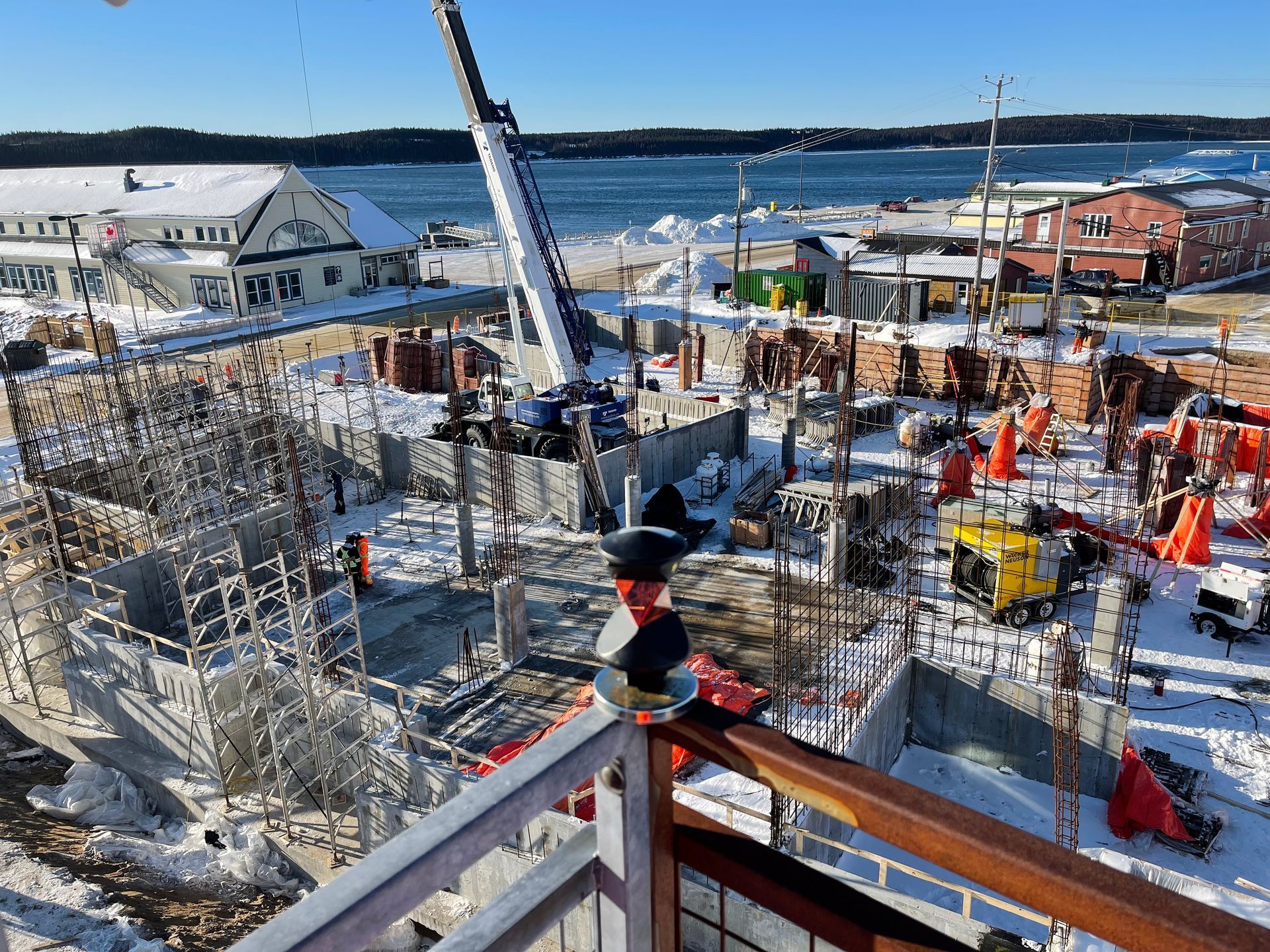 Chantier de construction enneigé en bord de mer avec grues, échafaudages et ouvriers près du port