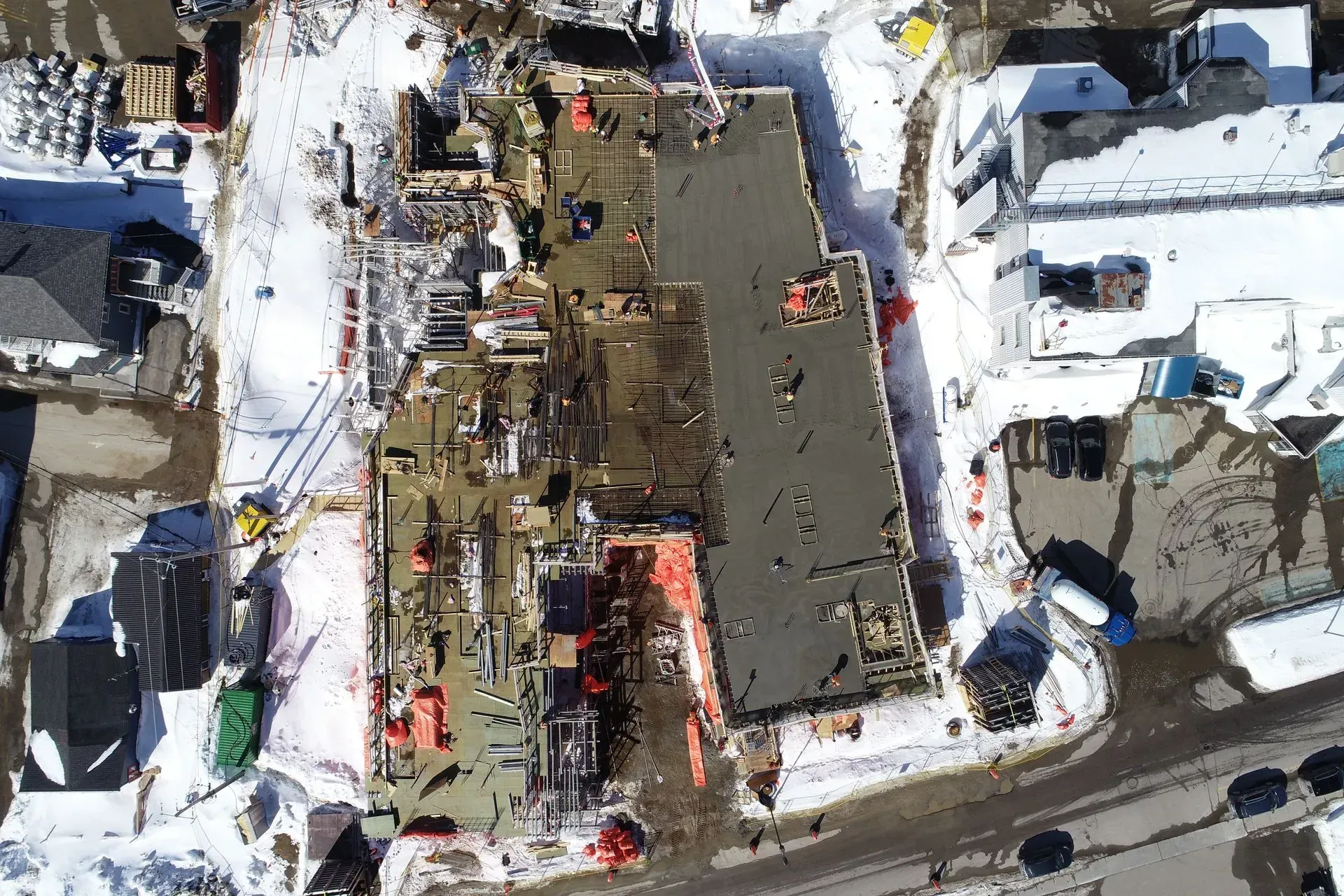 Vue aérienne d'un chantier enneigé montrant des fondations en béton partiellement achevées et des machines.