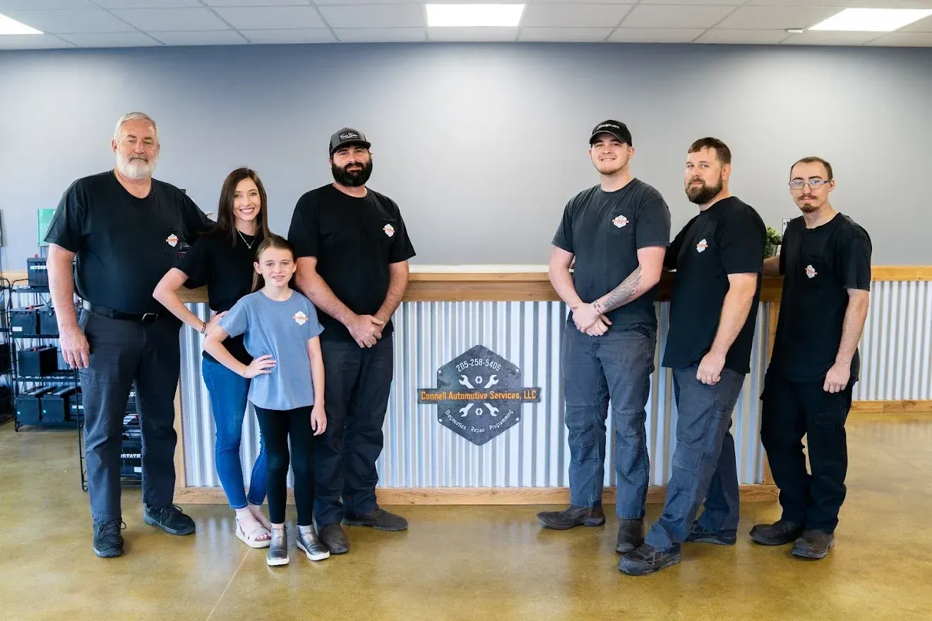 Six people standing indoors behind a wooden counter with a logo, wearing matching black shirts