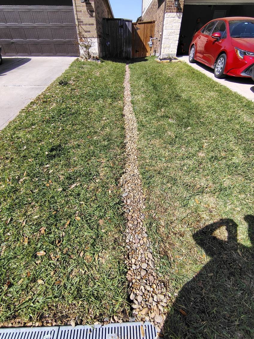 Lawn with stone-filled trench down the middle. Red car parked on the right. Shadow in the foreground.