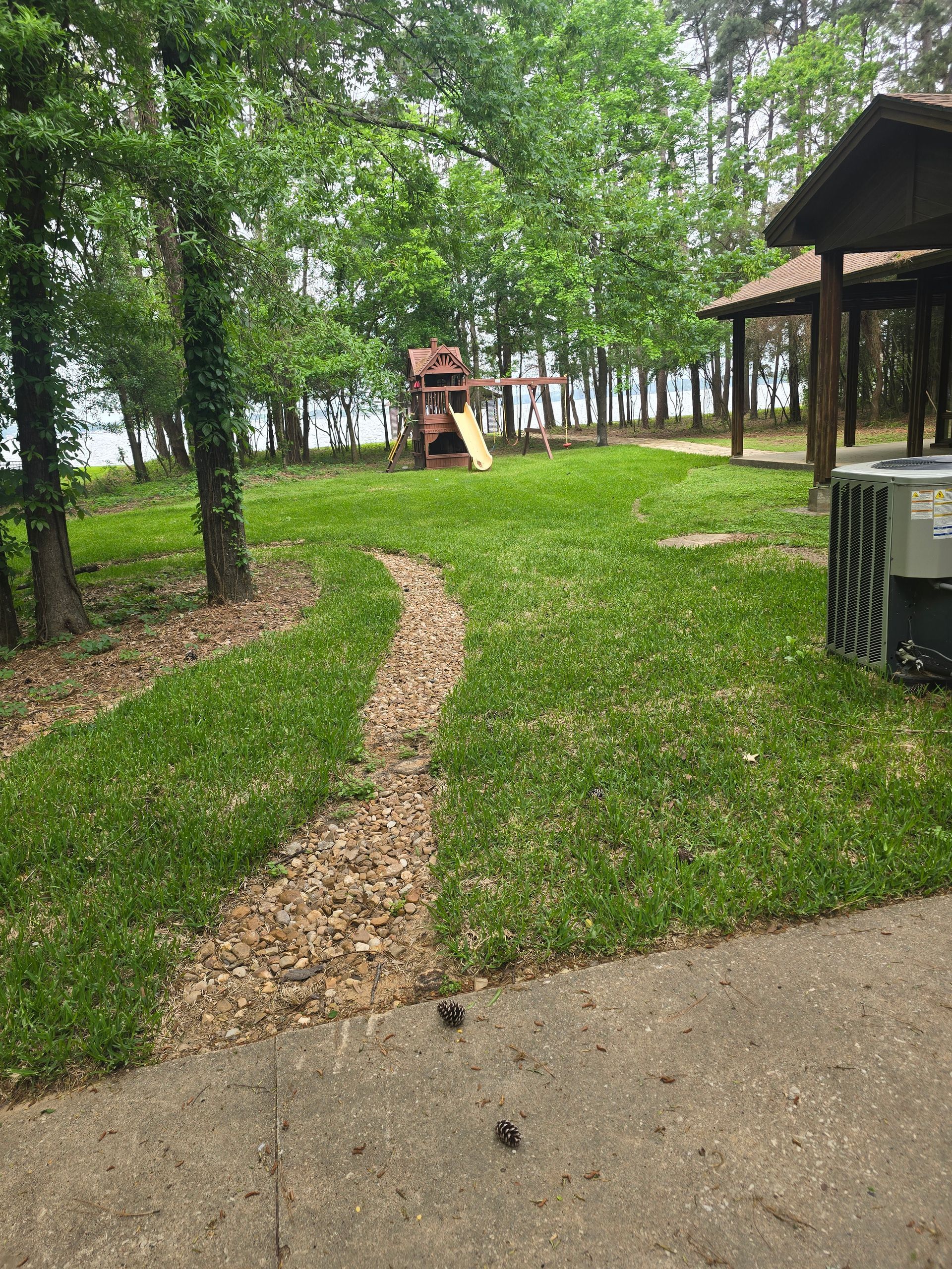 Grassy park area with a playground, trees, a pavilion, and a gravel pathway.