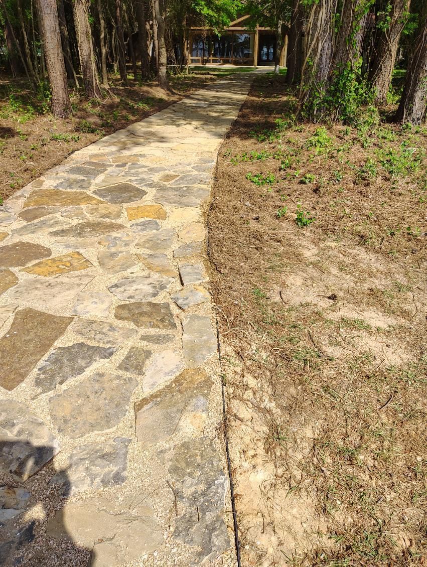 Stone path through trees leading to a building with a green roof.