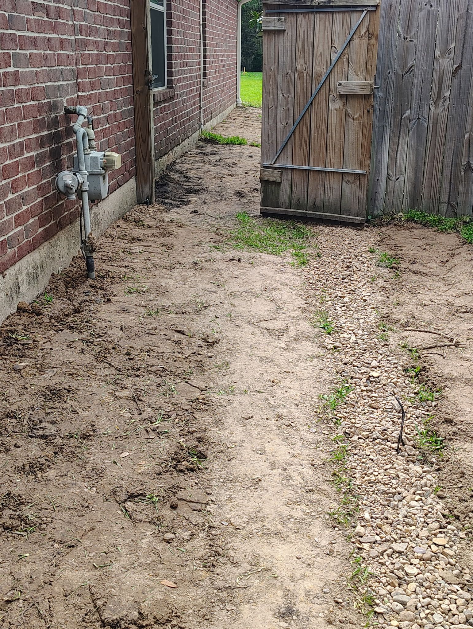 Dirt path between brick building and wooden door and fence.