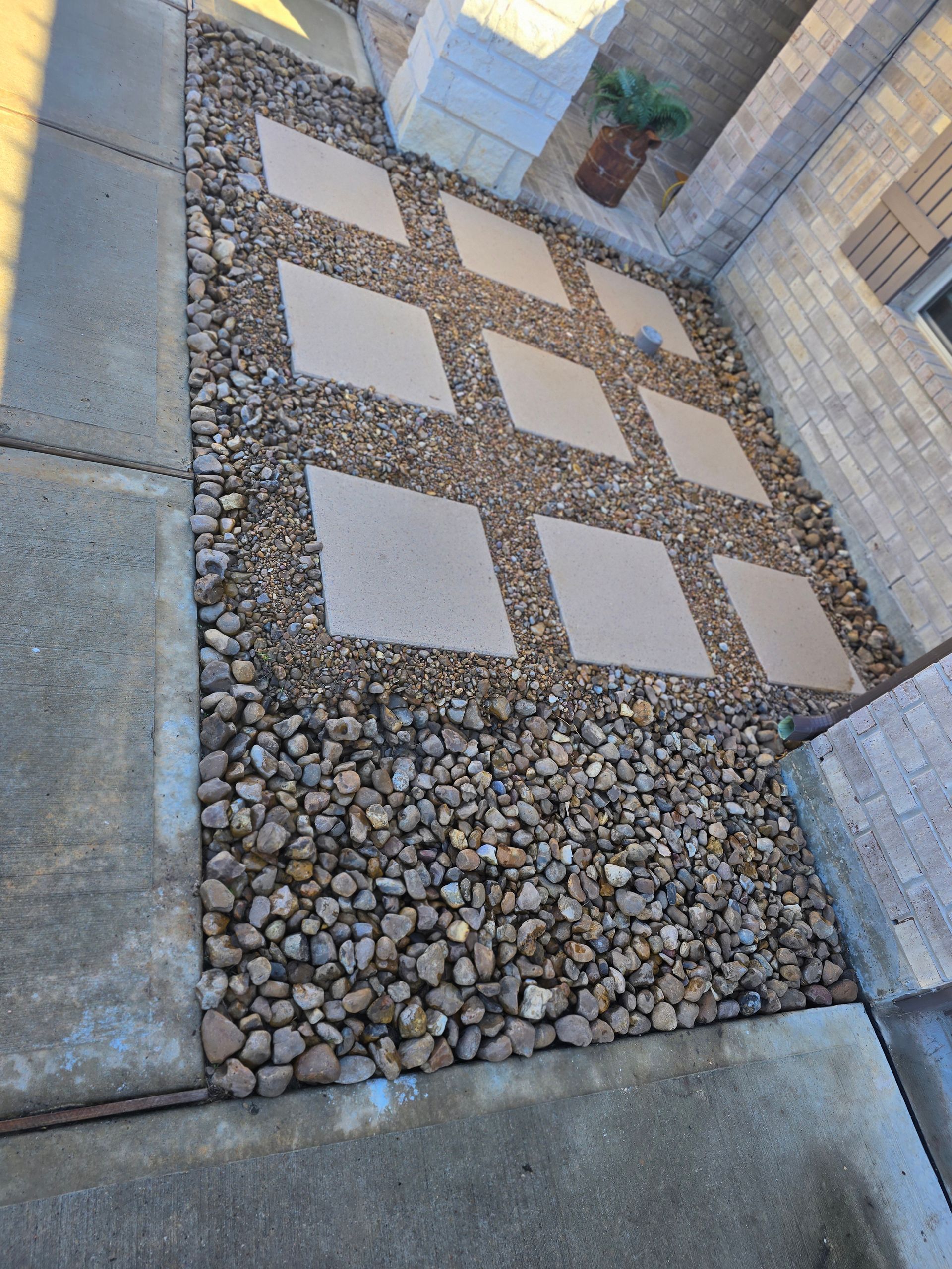 Gravel and stepping stones form a walkway between a concrete driveway and brick building entrance.