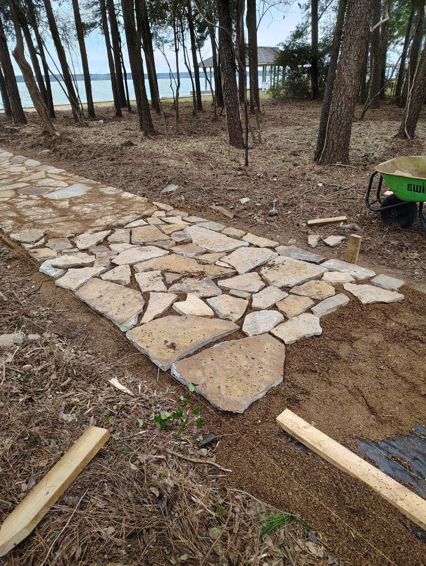 Stone pathway under construction in a wooded area near a body of water.