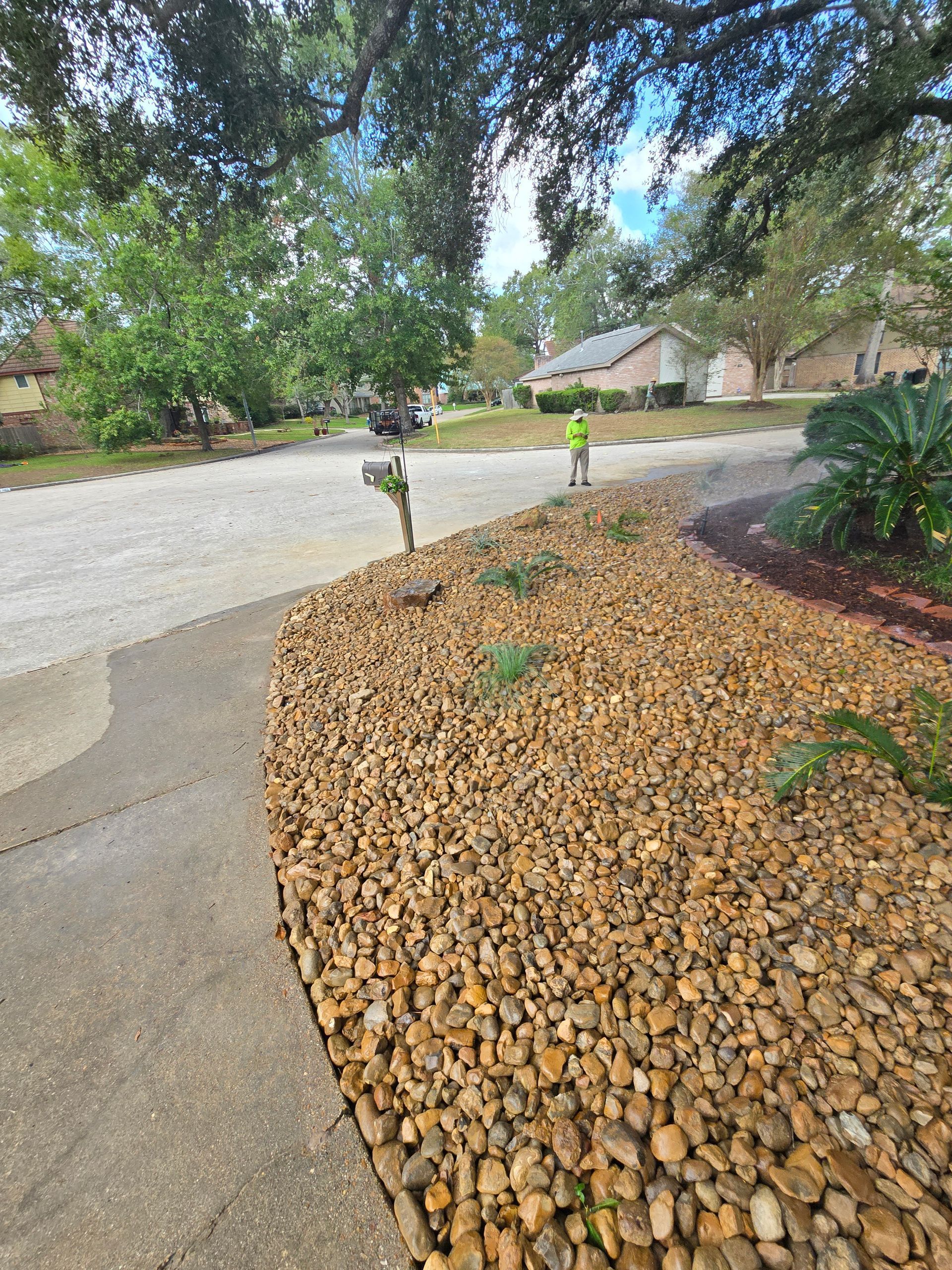 Gravel landscaping next to a sidewalk and street, with a person in the distance near houses.