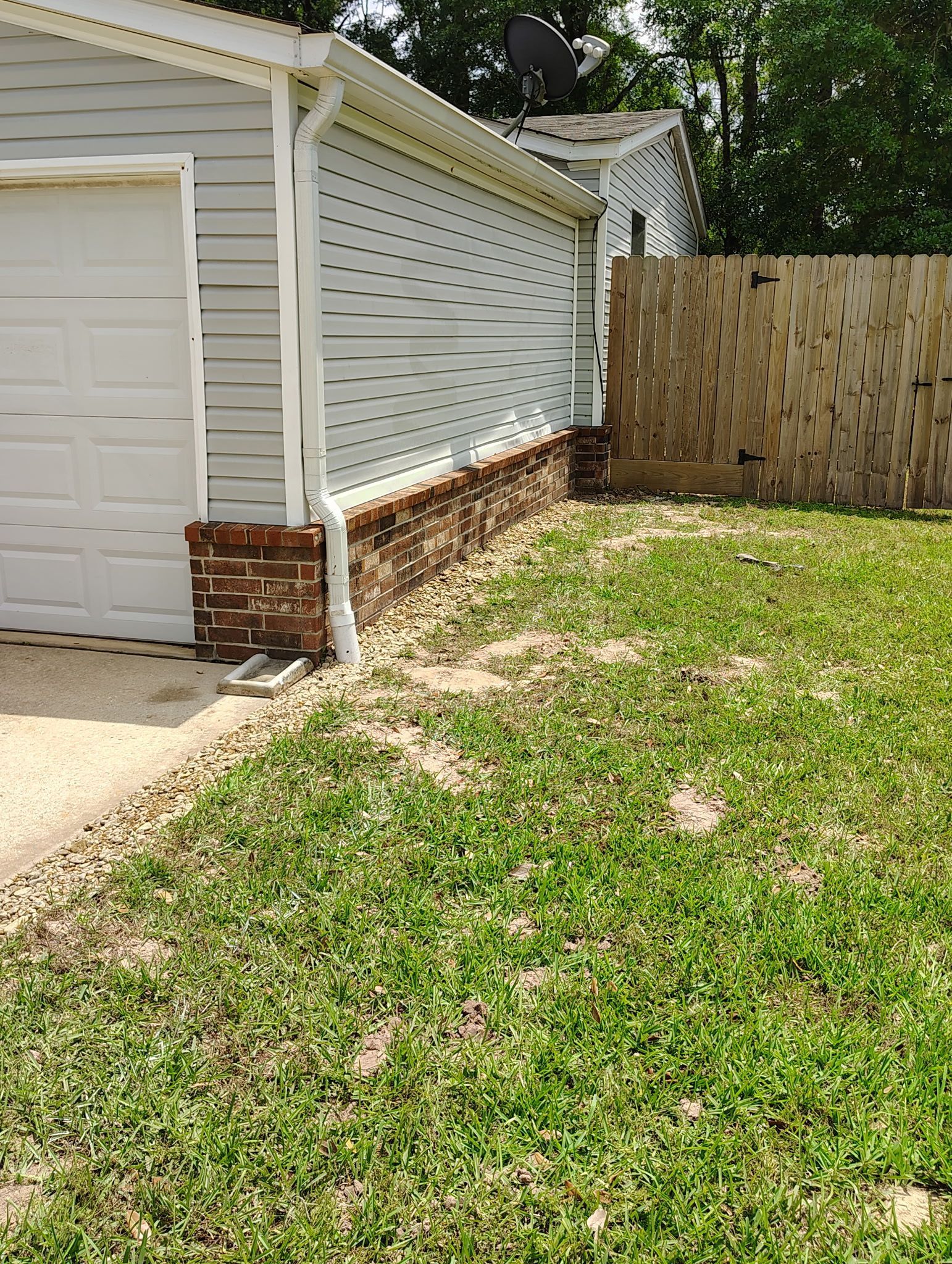 Garage exterior with a brick foundation and a wooden fence. Green grass and gravel are in front.