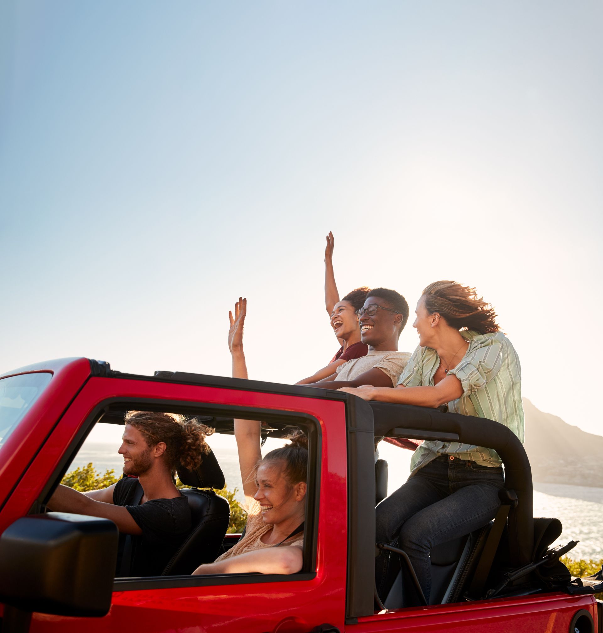 A group of people are riding in a red jeep