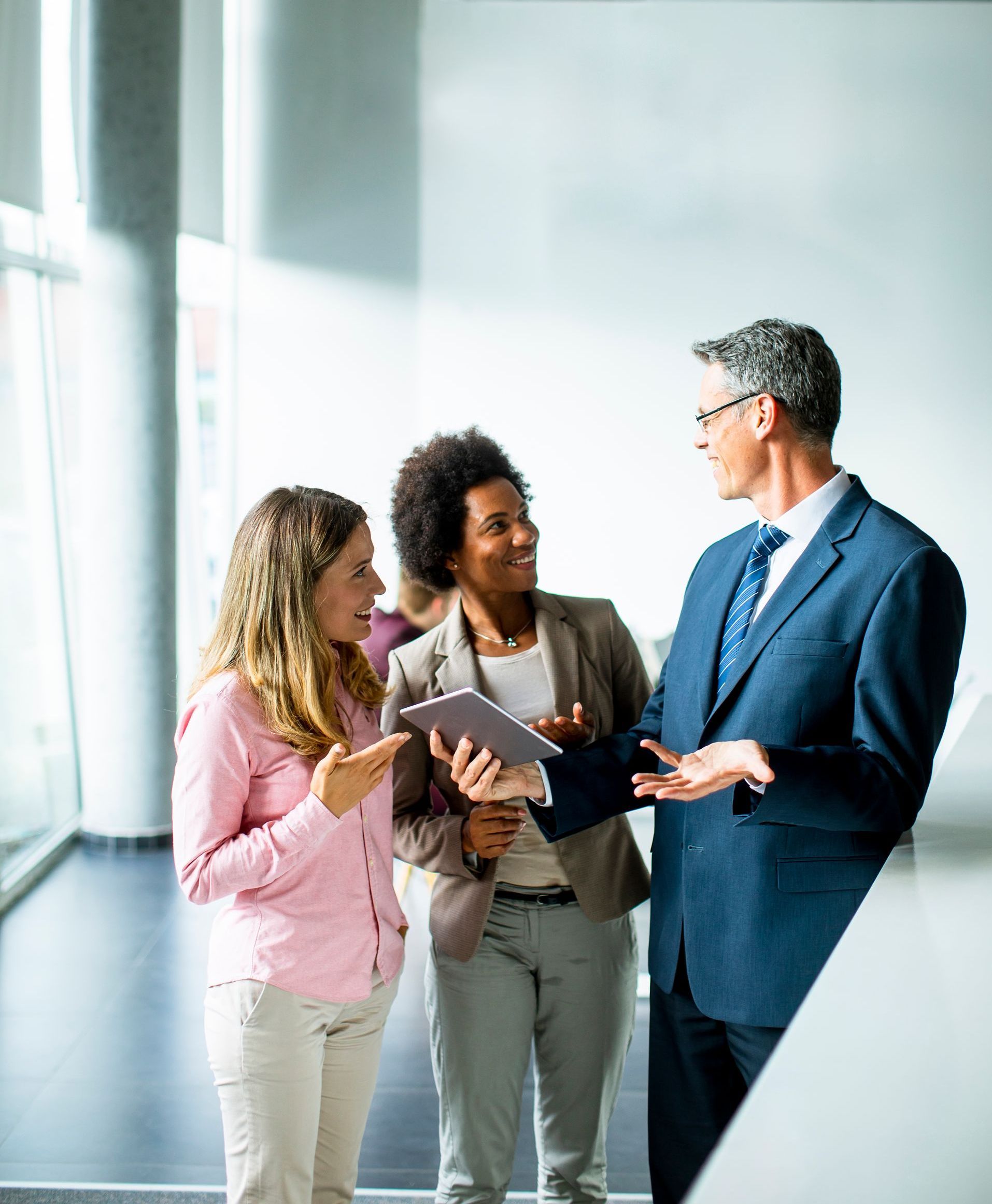 A man in a suit is talking to two women while holding a tablet.