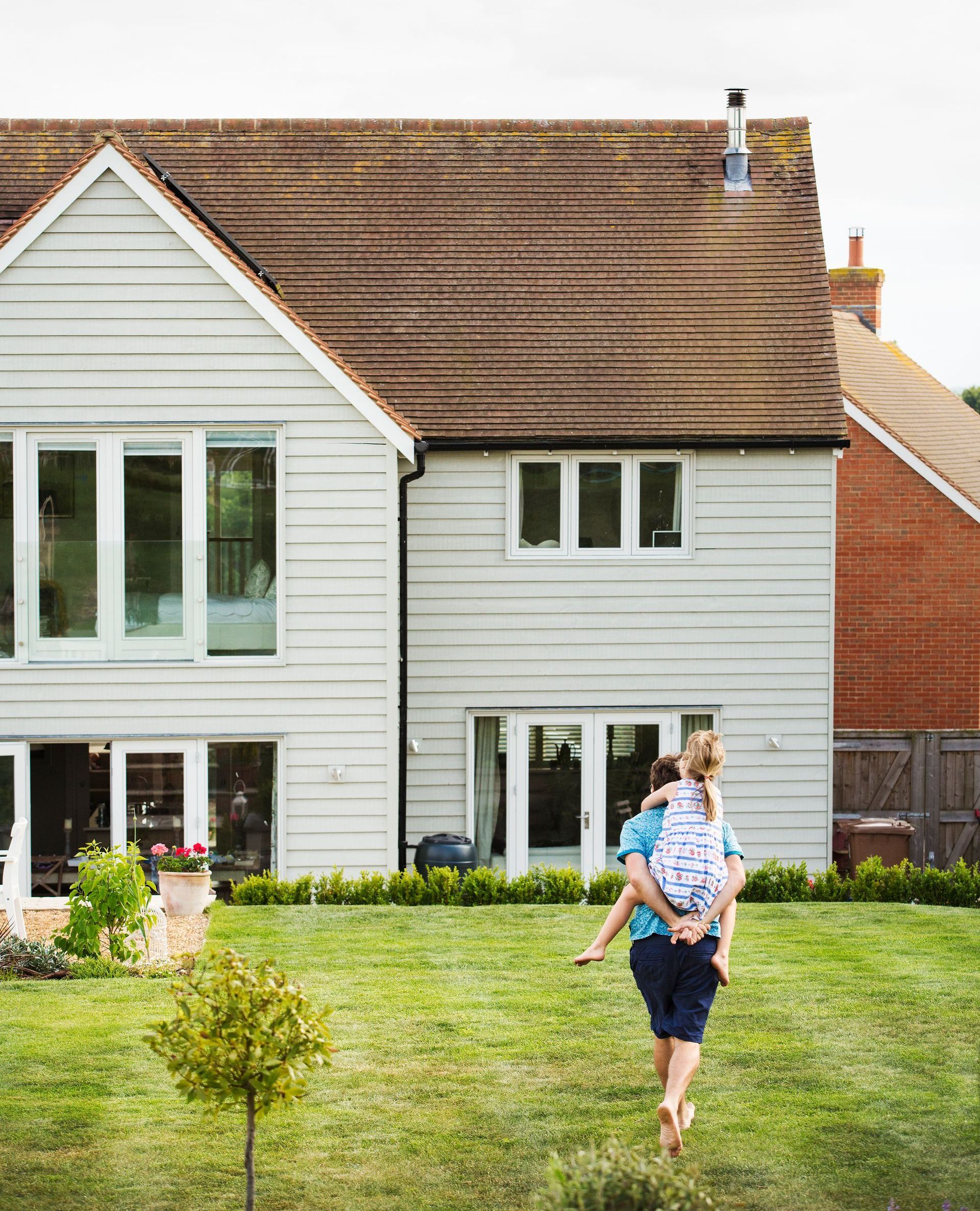 A man is carrying a child on his shoulders in front of a house.