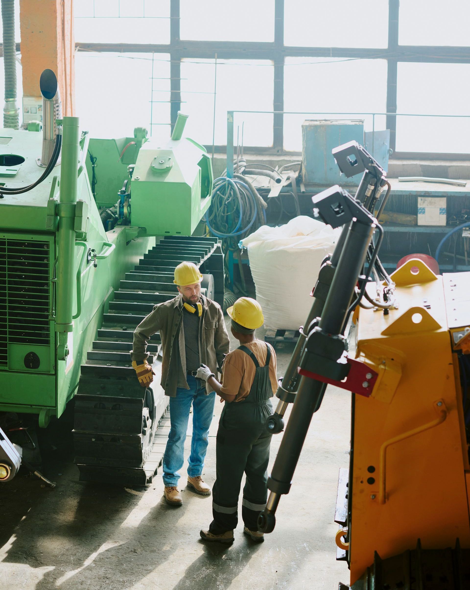 Two construction workers are standing in front of a machine in a factory.
