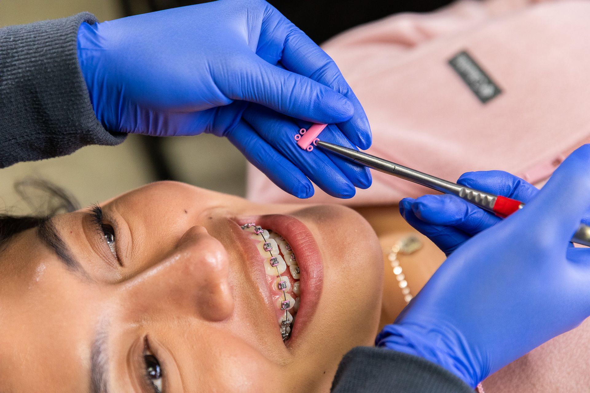 Person receiving orthodontic care; braces visible. Dentist using tool with pink rubber tip.