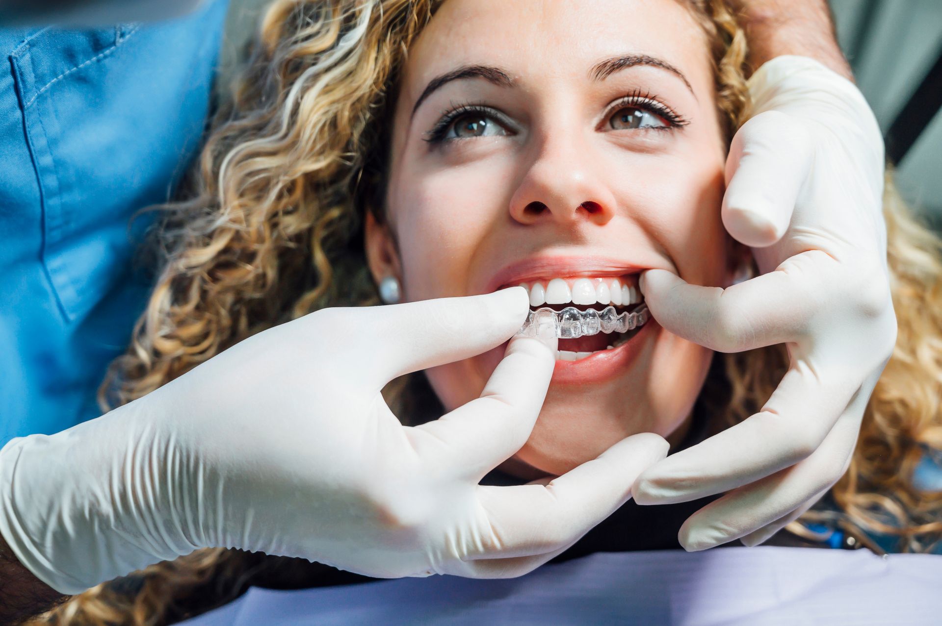 Dentist placing clear aligner in patient's mouth. Dental office setting, focused on the teeth.
