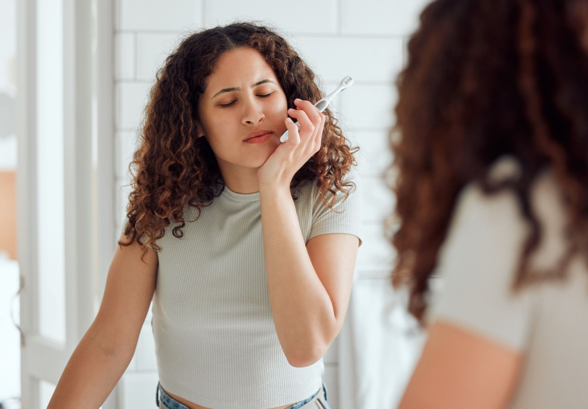 Woman touching her cheek while looking in a mirror in a bright bathroom