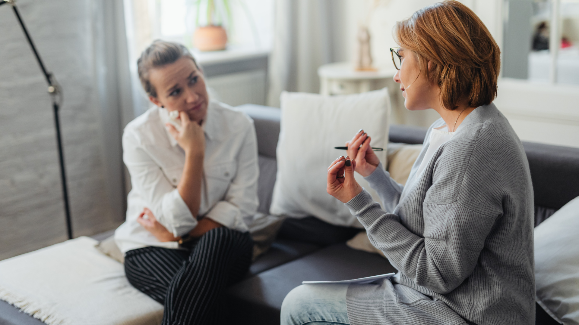 Woman in therapy session with therapist, discussing feelings on a sofa.