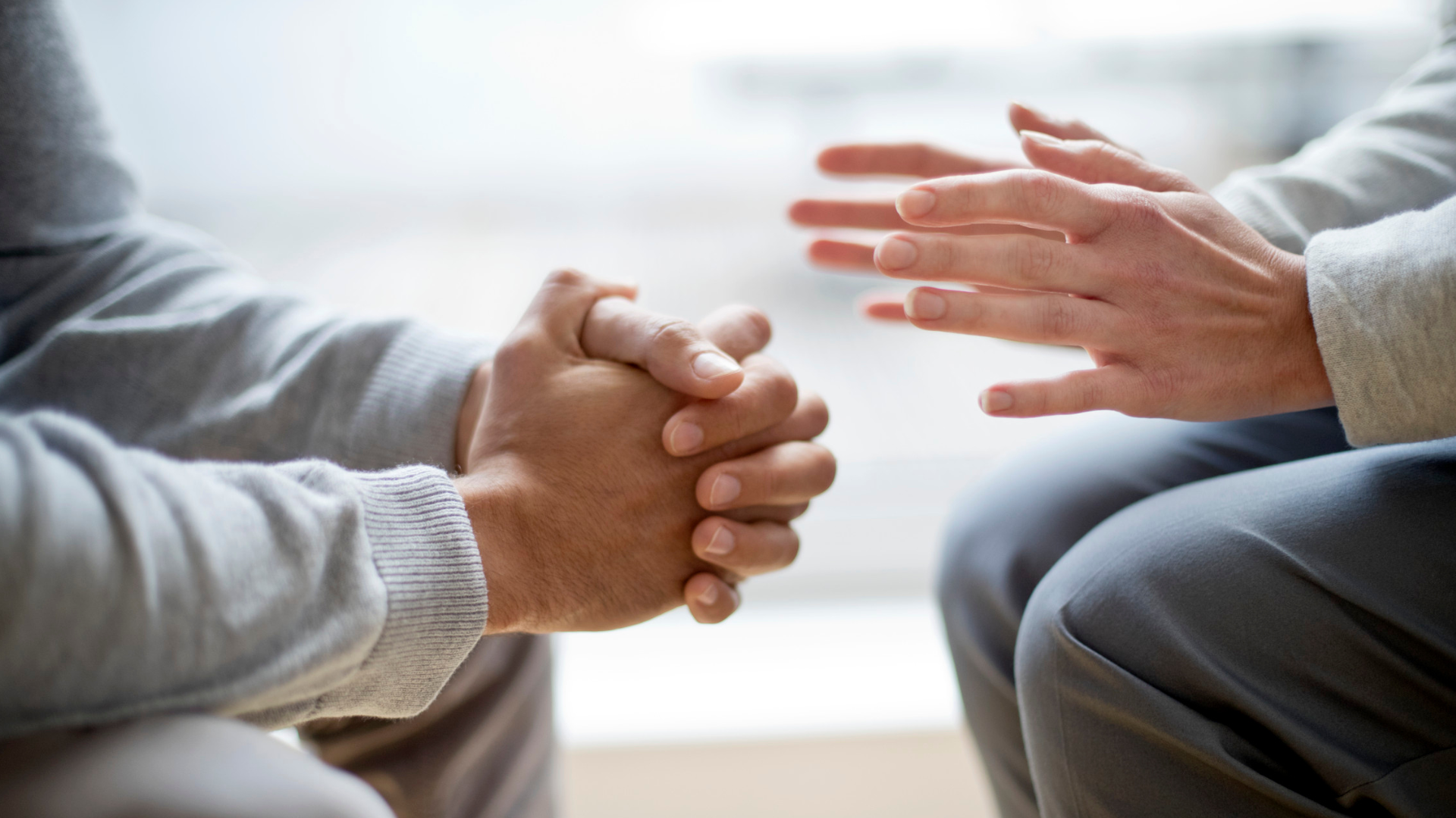 Two people in conversation; one with clasped hands, the other with hands open in a gesture.
