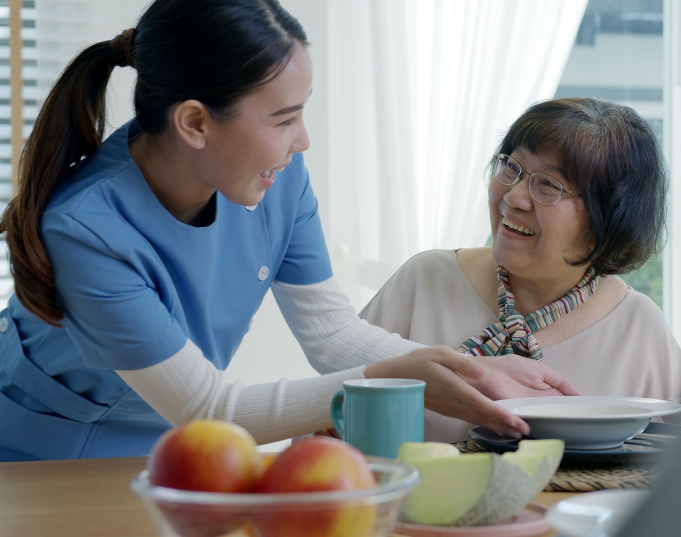 A healthcare provider in blue scrubs discusses information on a tablet with an elderly woman in a clinic.