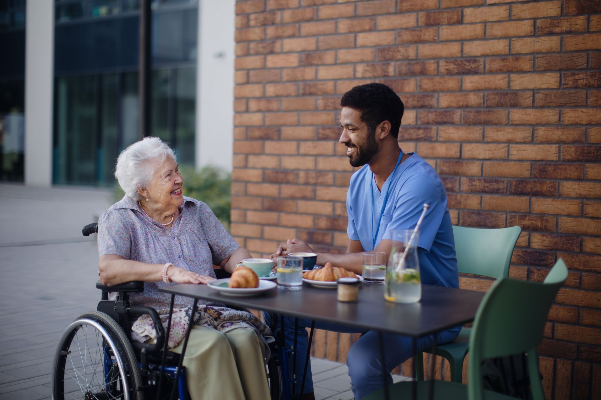 A smiling healthcare worker assists an elderly man using a walker in a bedroom. They are looking at the camera.
