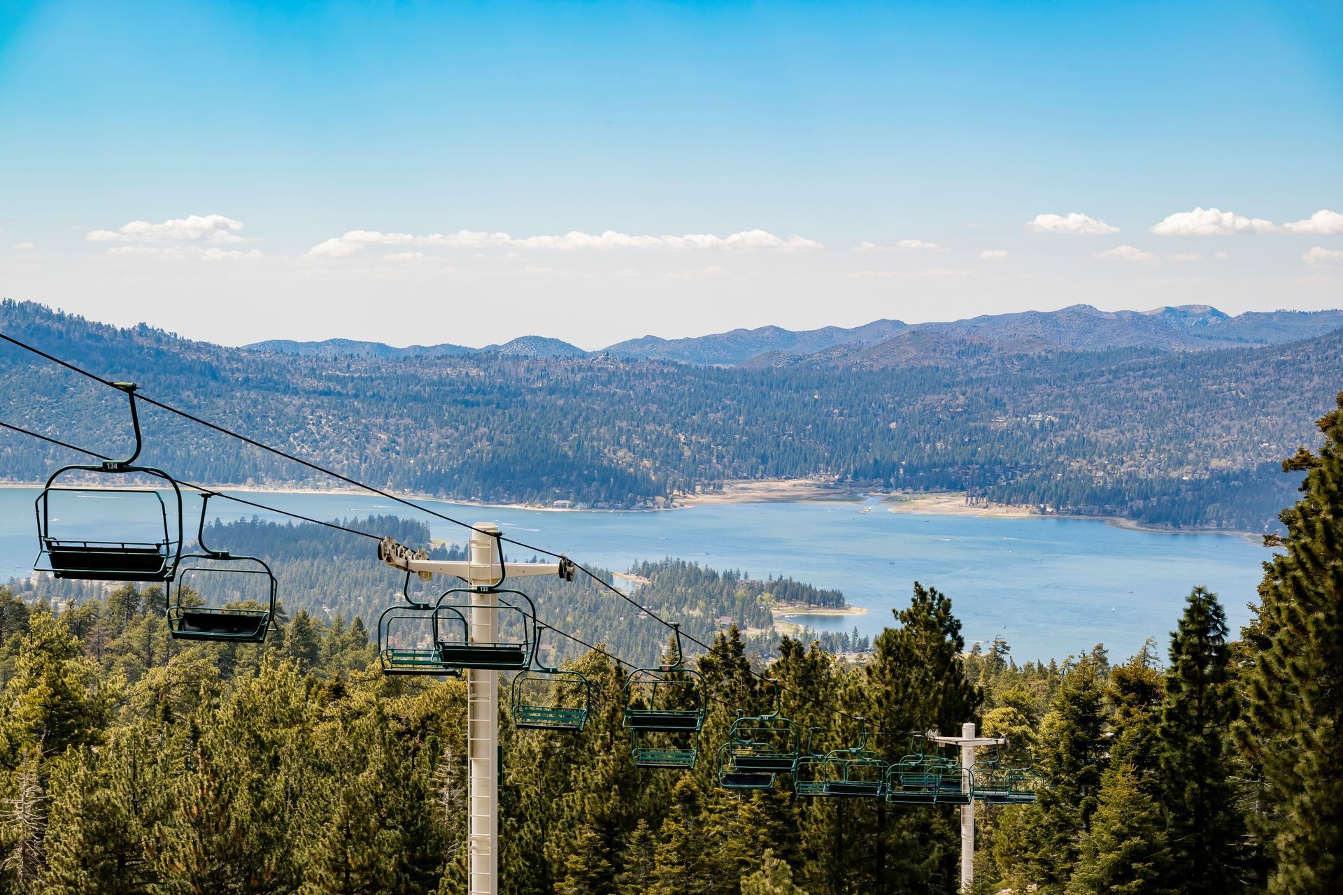 Ski lift overlooking a lake surrounded by forest on a sunny day.