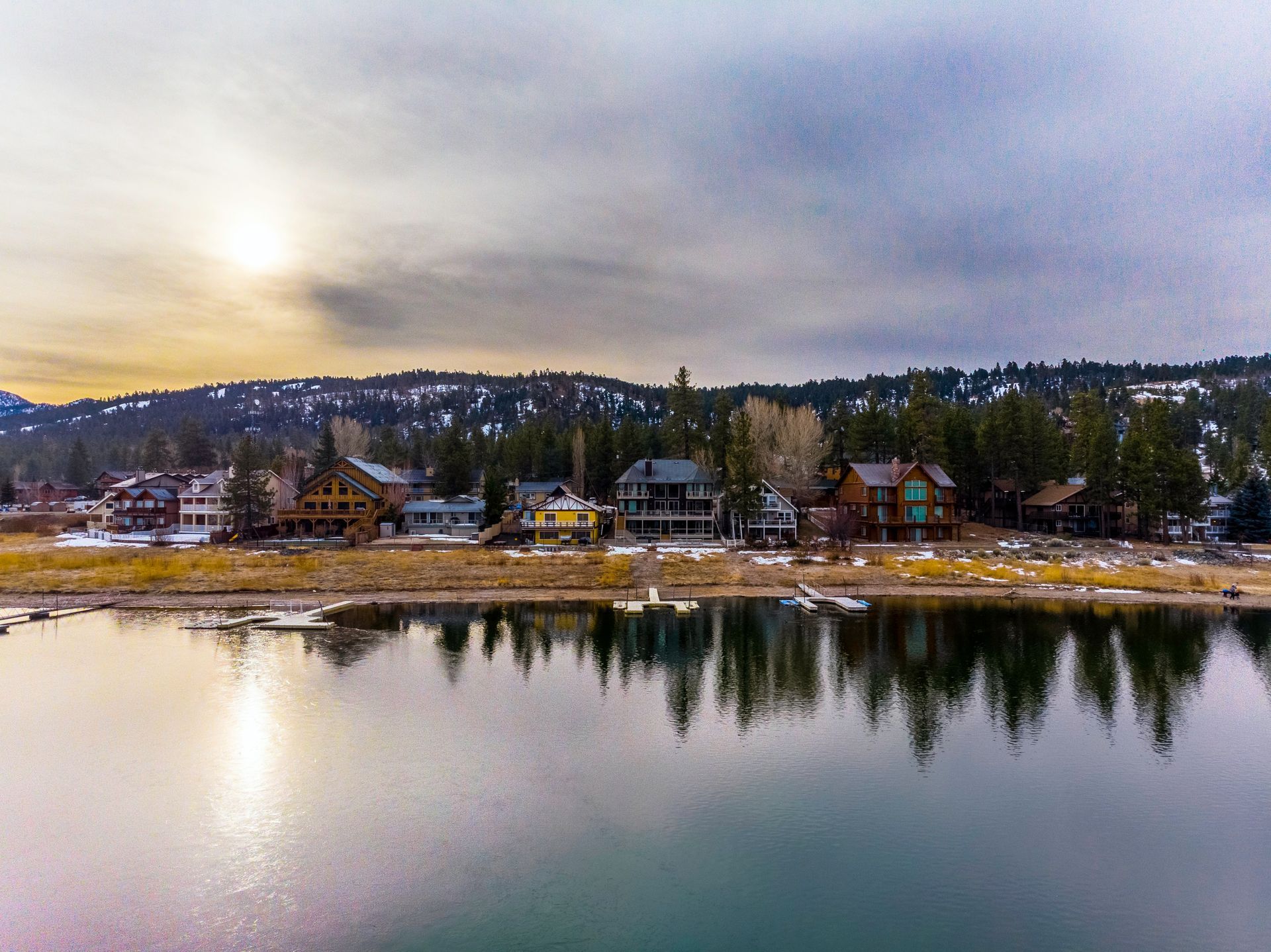 Lakeside homes along a shoreline, under a cloudy sky. Trees and a small mountain visible in the background.