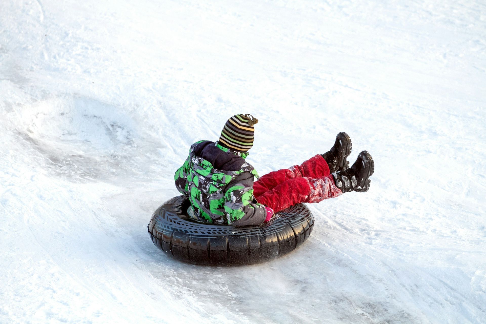 Child riding a snow tube down a snow-covered hill, wearing winter clothes.