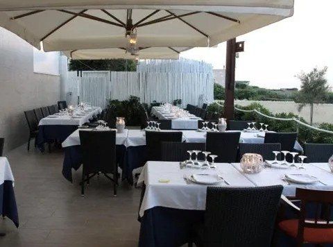 Terrazza esterna del ristorante con tovaglie bianche, sedie nere, ombrelloni e vista sul giardino.