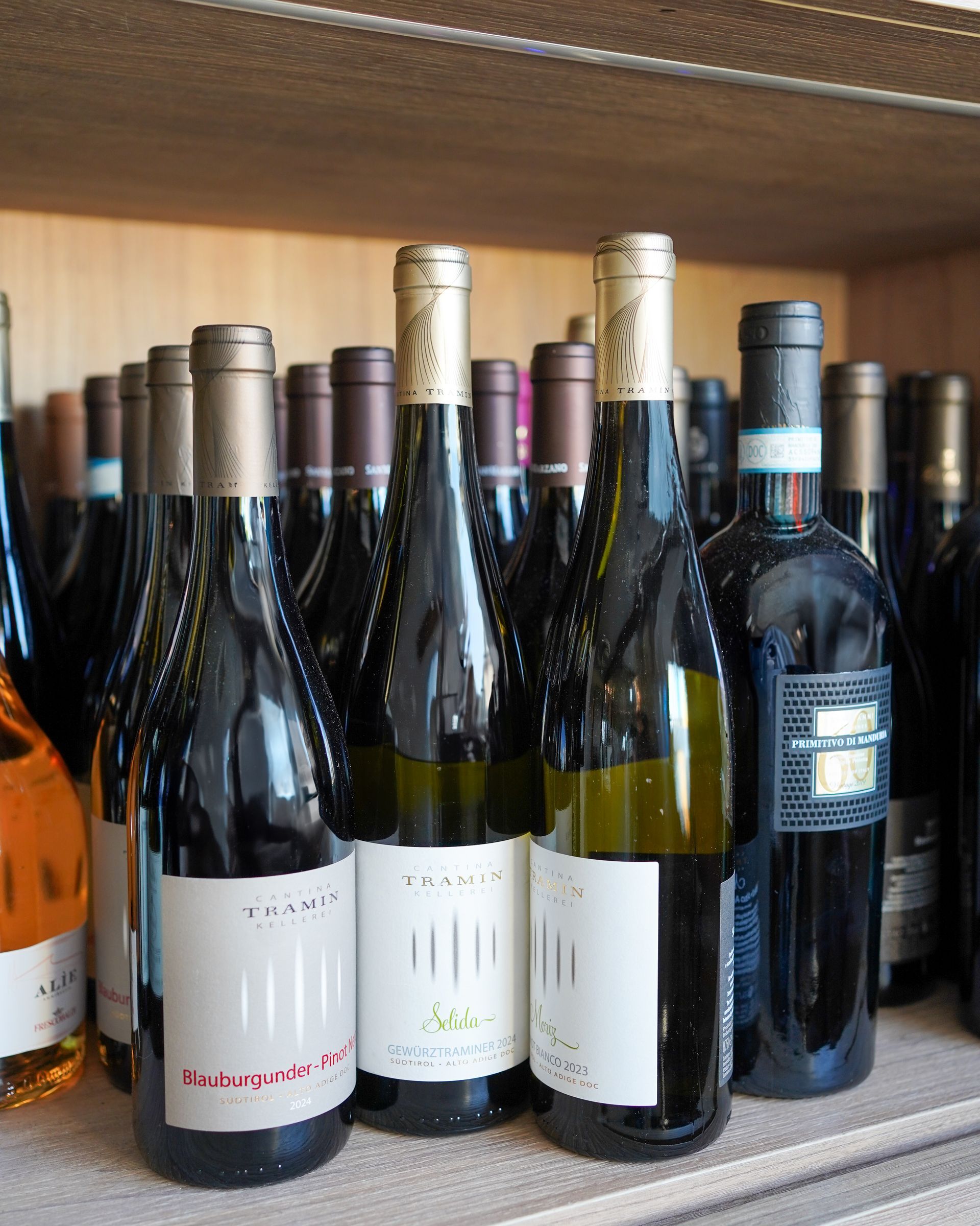 Diverse bottiglie di vino allineate su uno scaffale di un negozio, con etichette di vino bianco, rosso e rosato ben visibili.