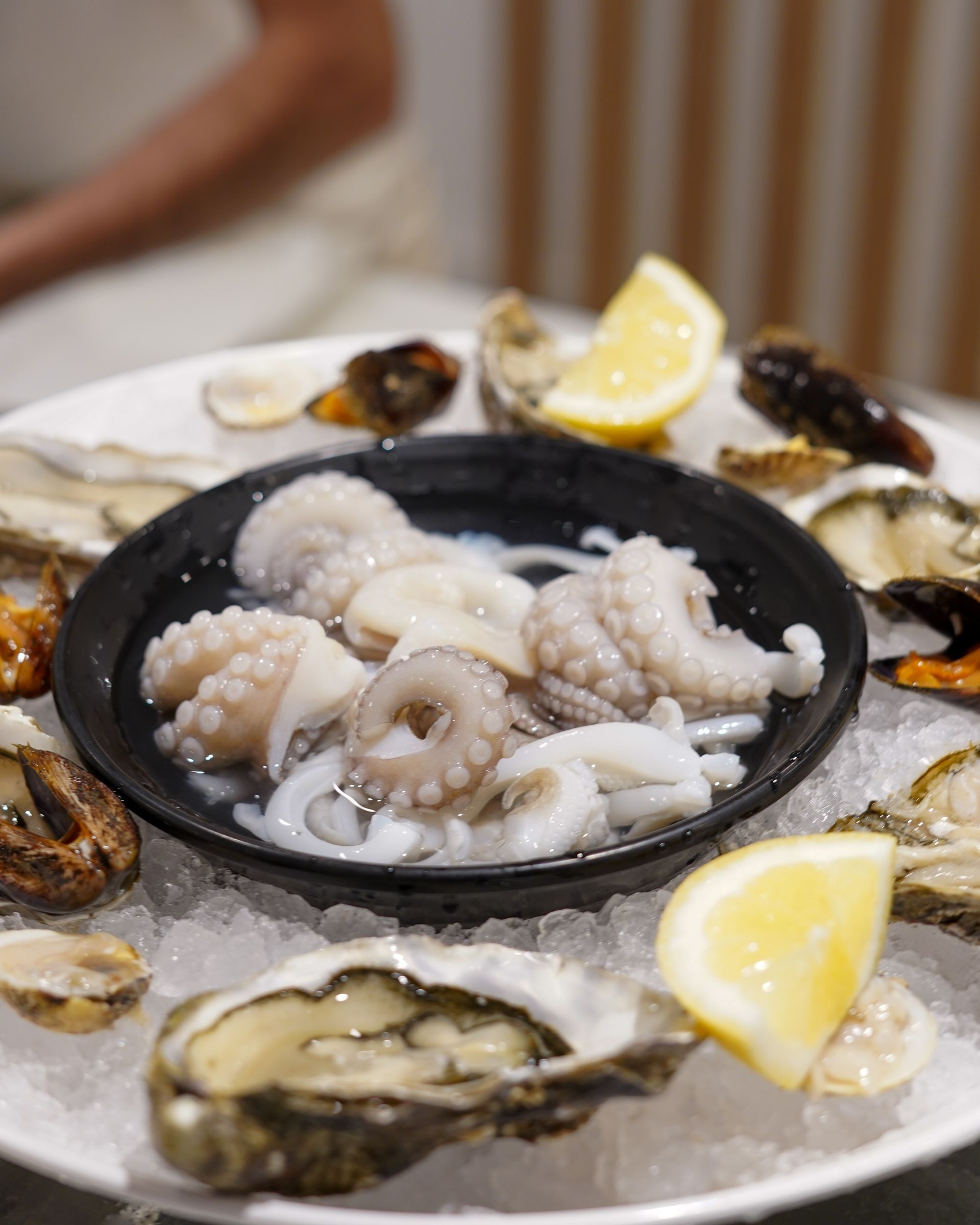 Piatto di frutti di mare con ostriche, spicchi di limone e una ciotola di polipetti in brodo