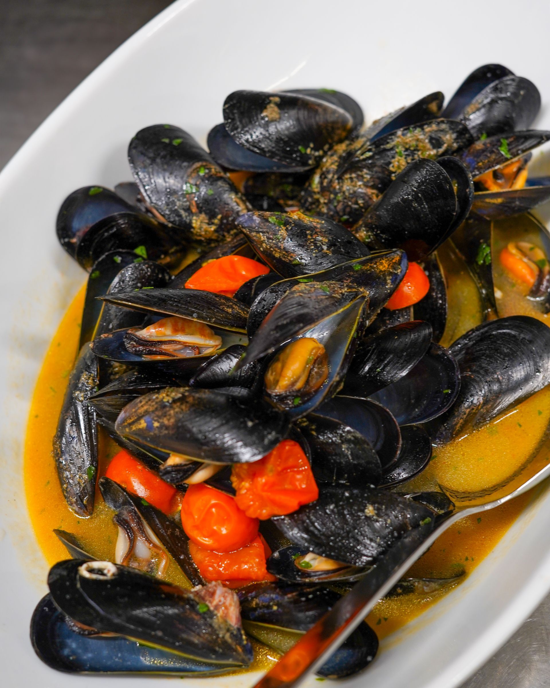 Cozze in brodo con pezzetti di peperone rosso in una ciotola bianca.