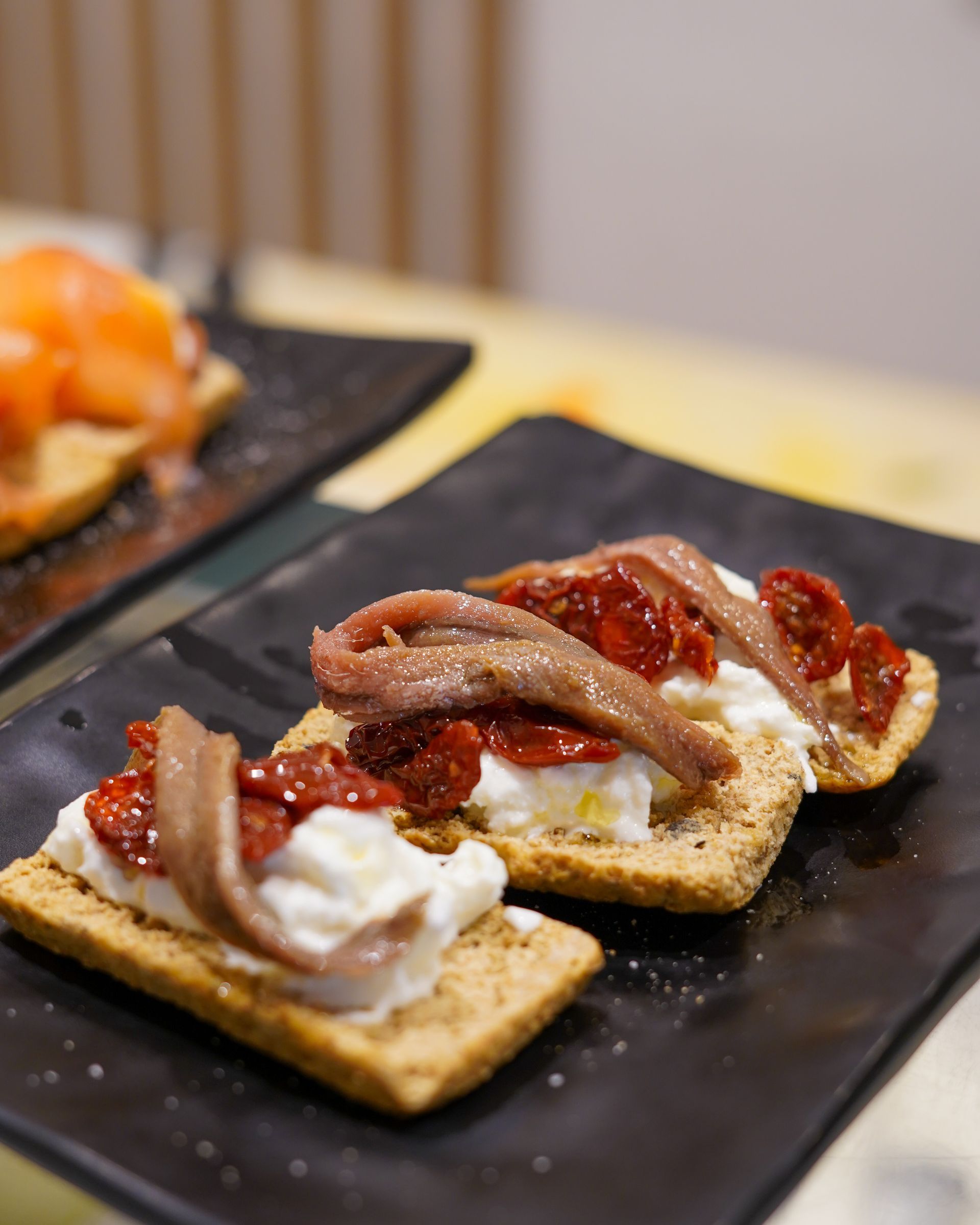Crostini con crema bianca, salsa di pomodoro e acciughe su un piatto nero.