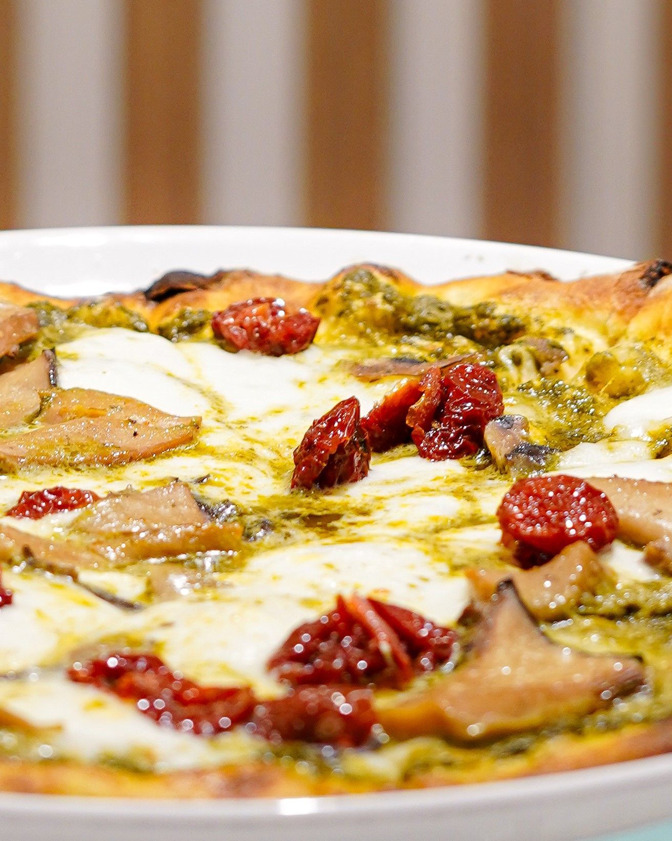 Pizza al formaggio con peperoni rossi e pesto verde su un piatto bianco