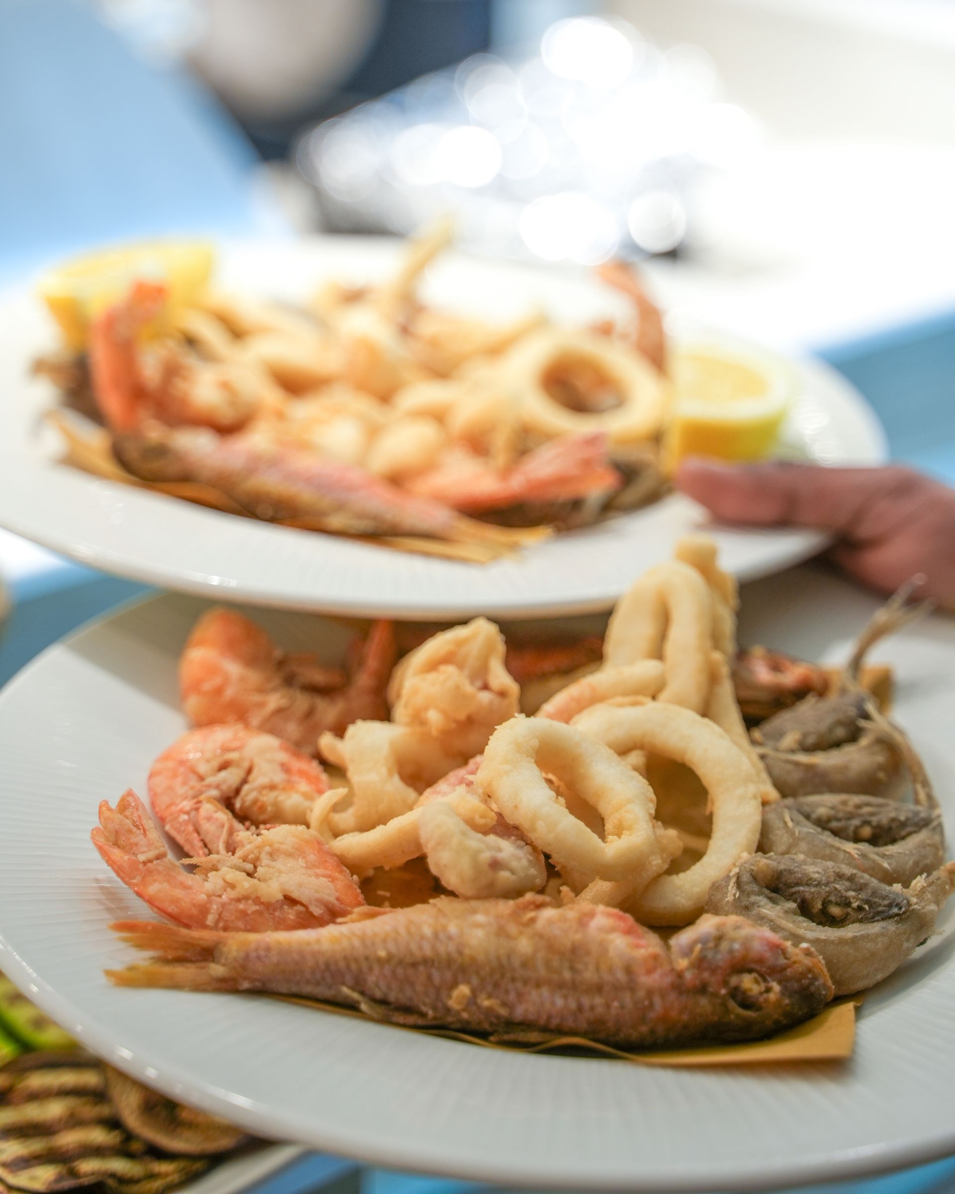 Piatto di frutti di mare fritti – gamberi, anelli di calamari e pesce – servito su un piatto bianco con una mano che si protende dal lato